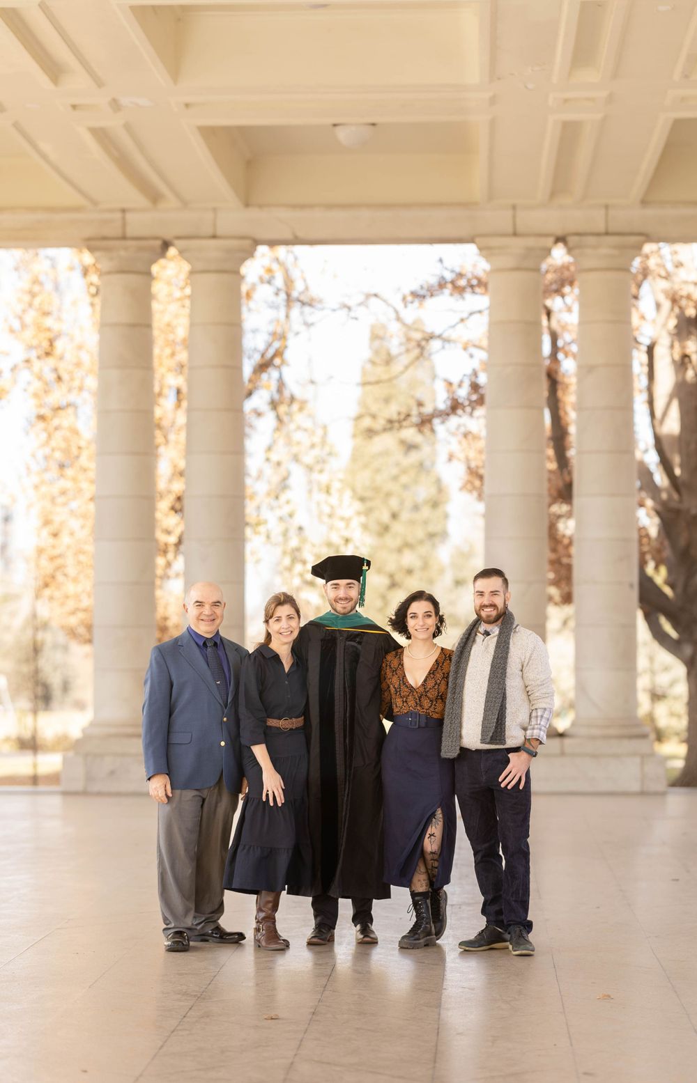 Family graduation portrait under white columns with golden autumn background.