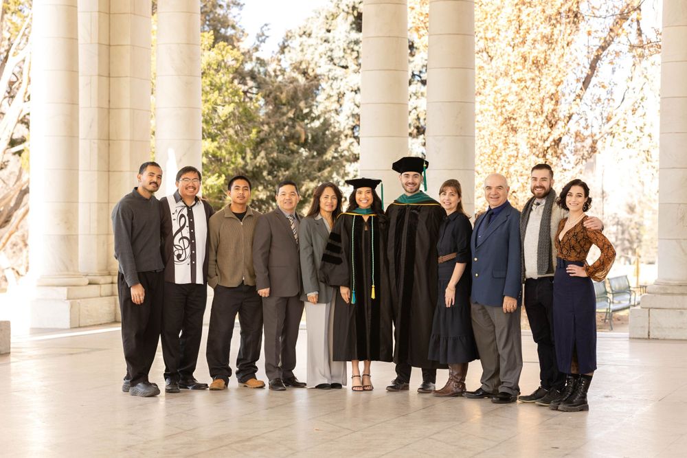 Large family group photo with graduate in black robe under white columned portico.