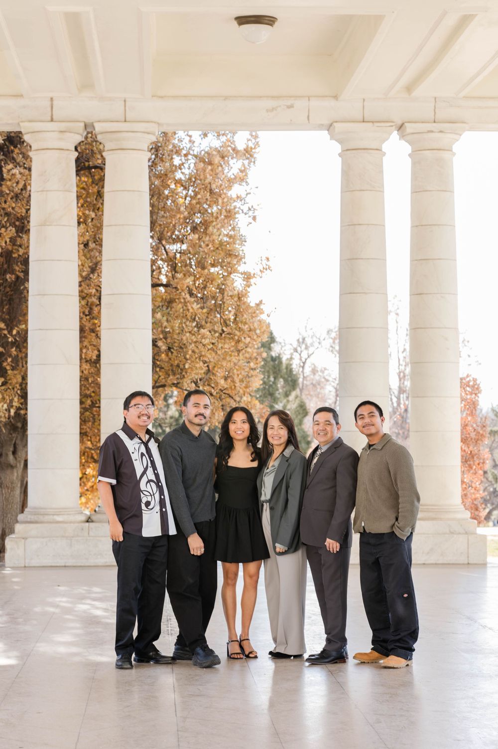 Professional group photo of six people under white columns with autumn foliage.