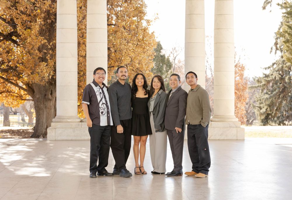 Group portrait of six people standing under white columns with fall colors in background.