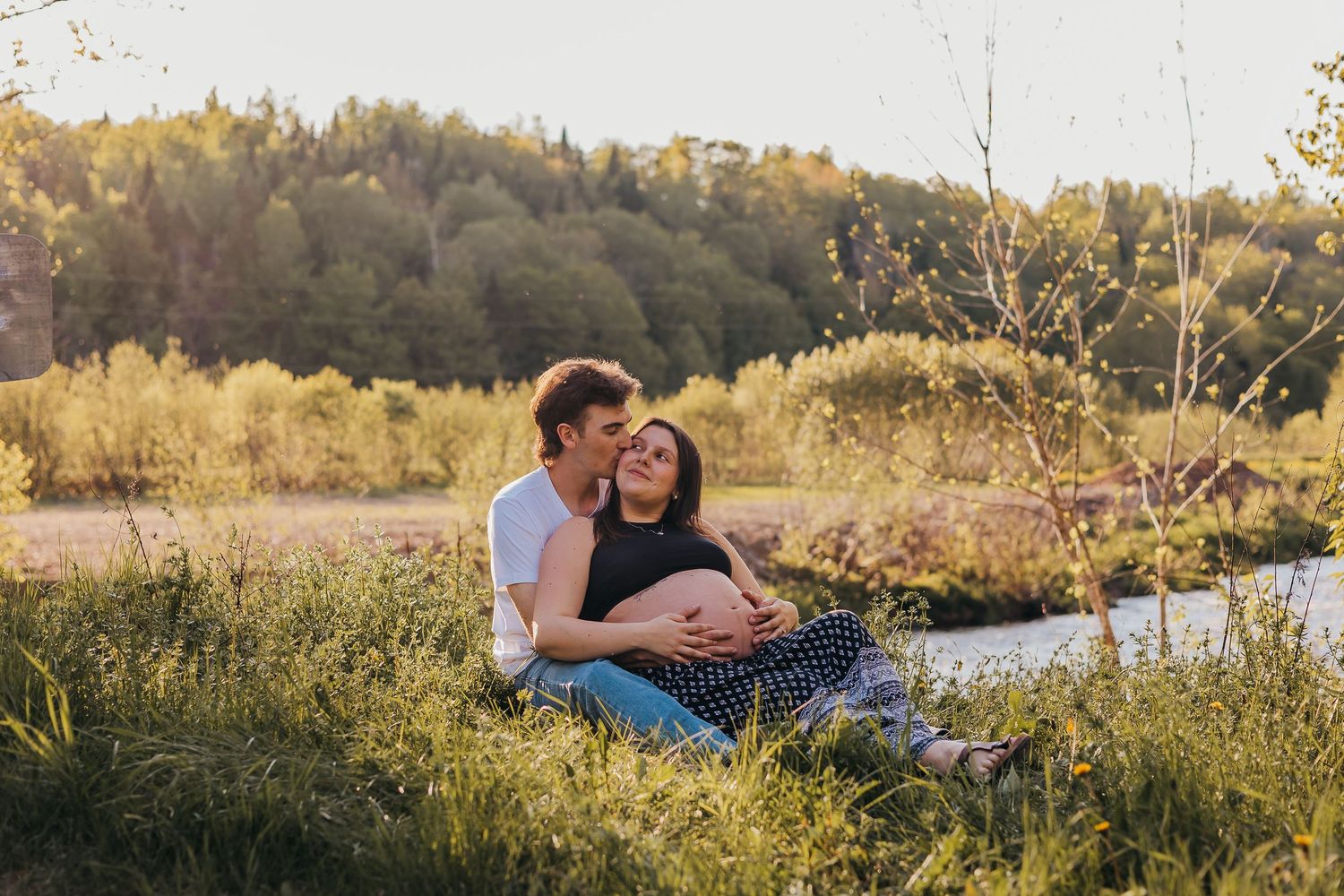 Expectant couple poses with their fluffy goldendoodle dog on nature path.