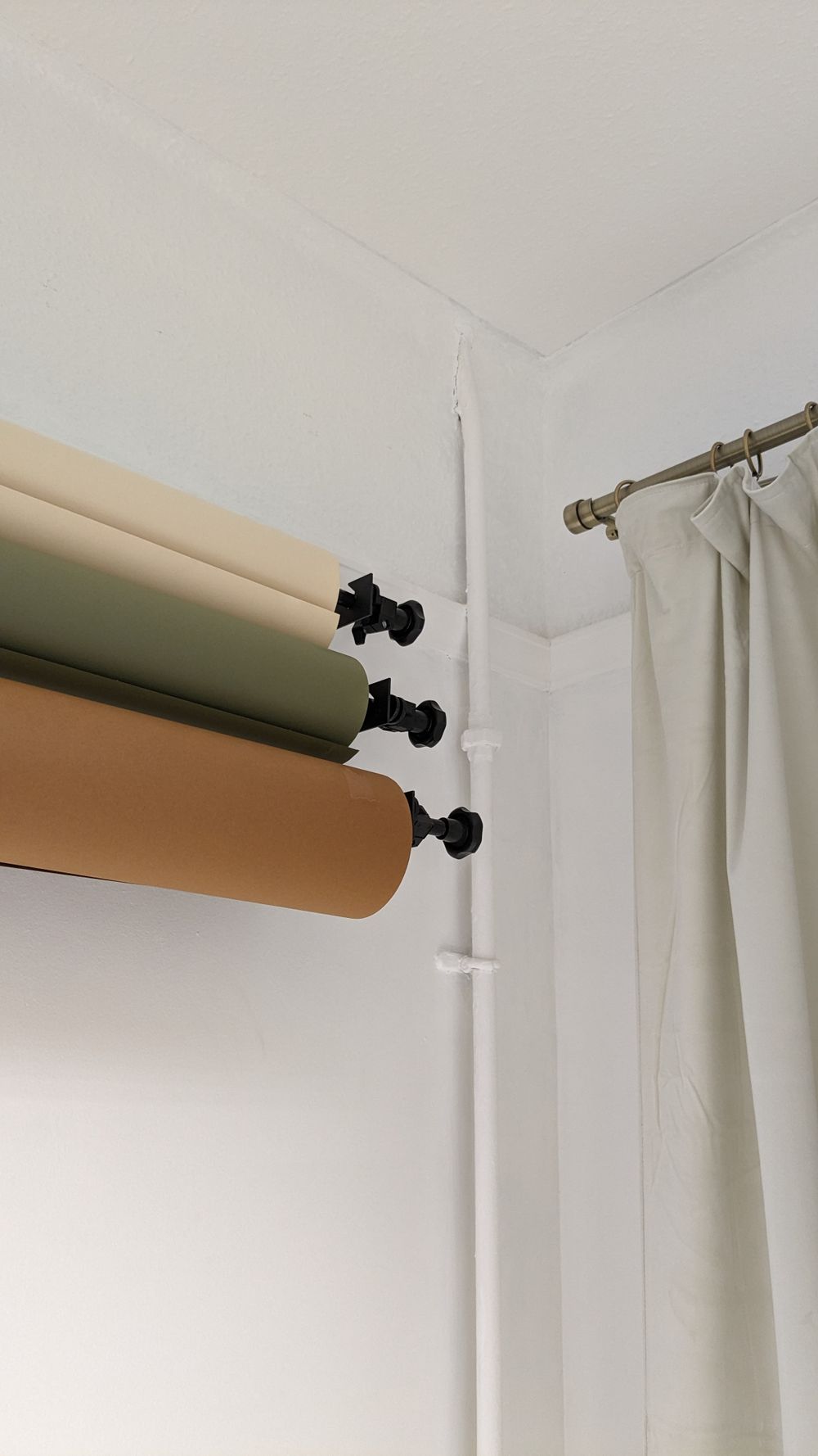 Photography backdrop setup showing mounted paper rolls and curtain rod against white wall.