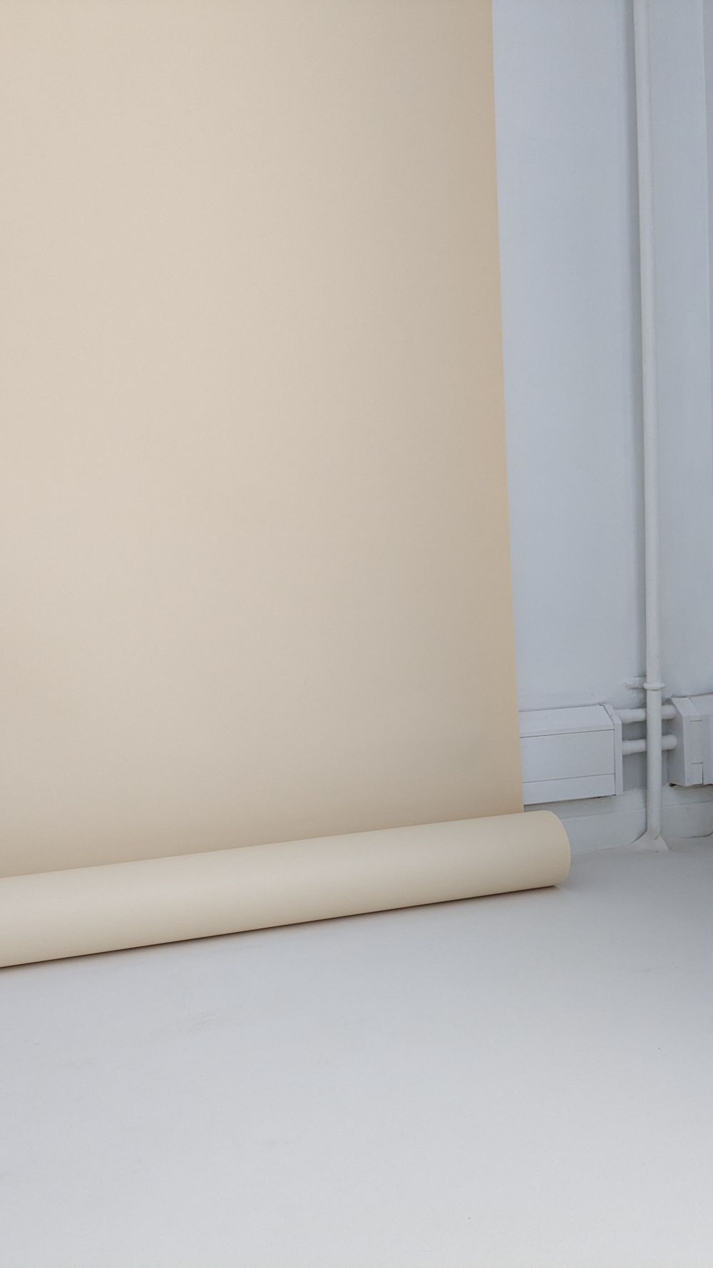 A minimal studio setup with cream colored seamless backdrop paper roll against white walls and floor.