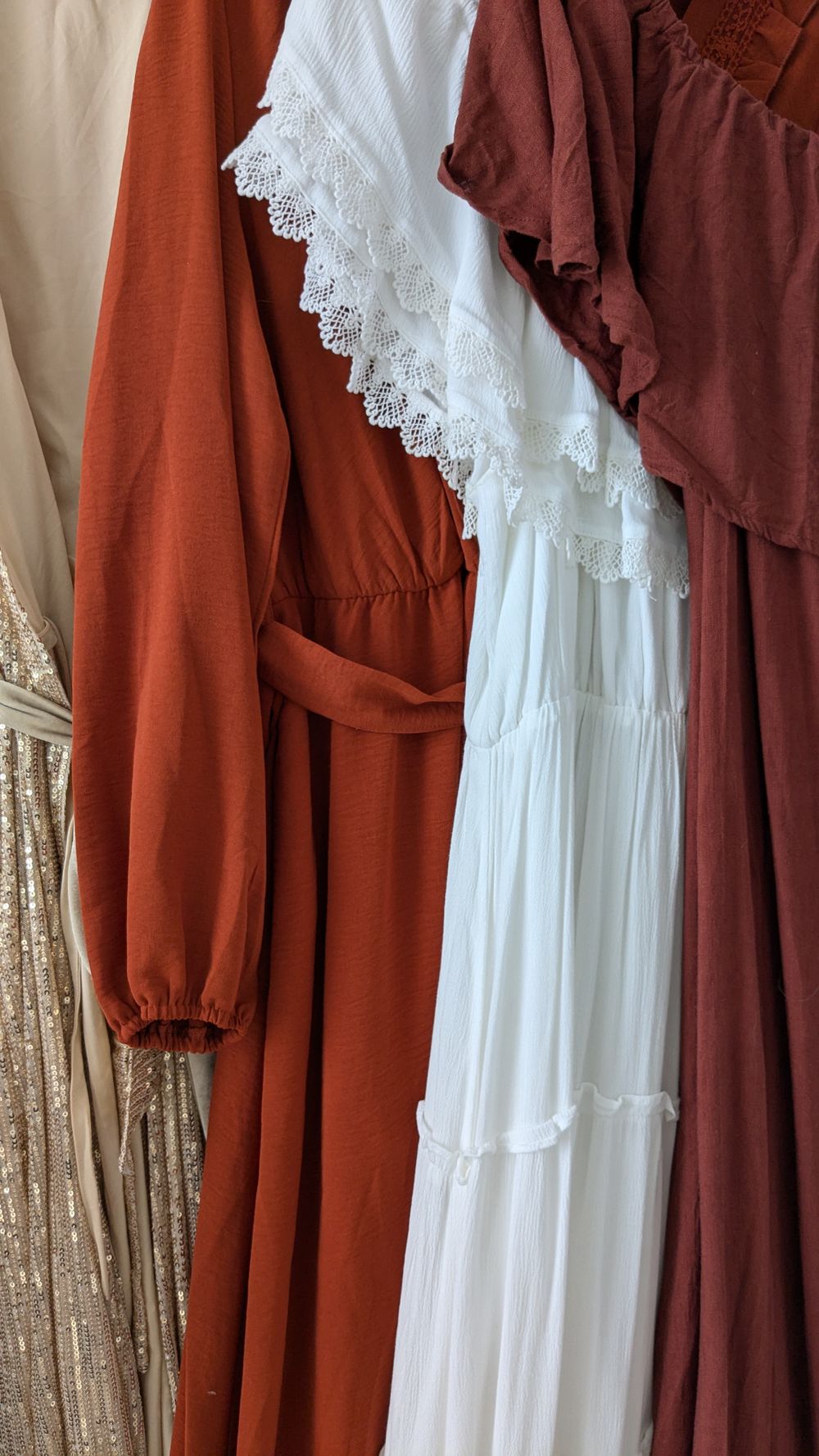 Hanging dresses in warm autumn tones featuring a white lace-trimmed dress between rust and brown colored garments.