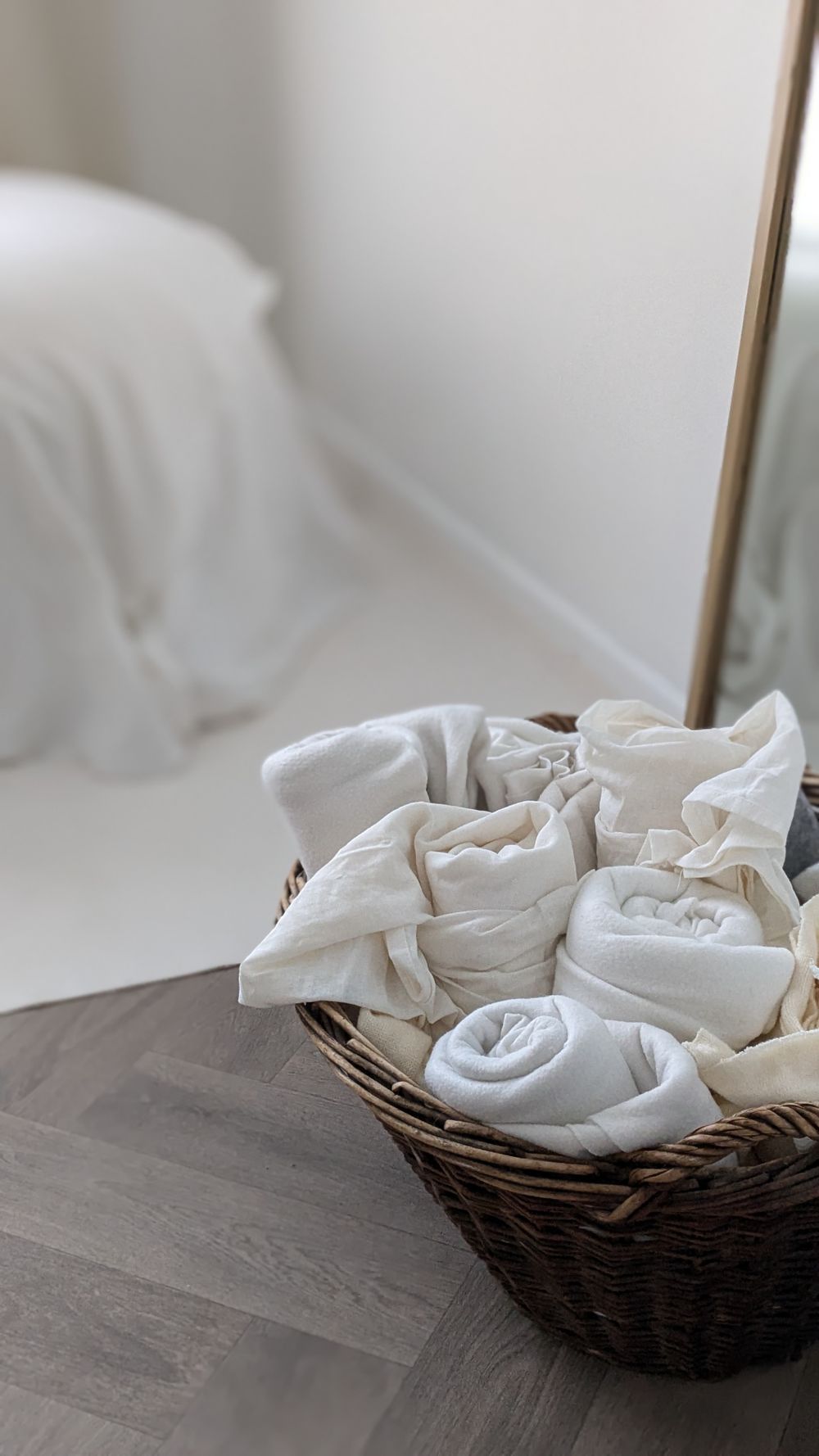 A wicker basket filled with rolled white blankets sits on a dark wooden surface beside a newborn posing beanbag with white linens.