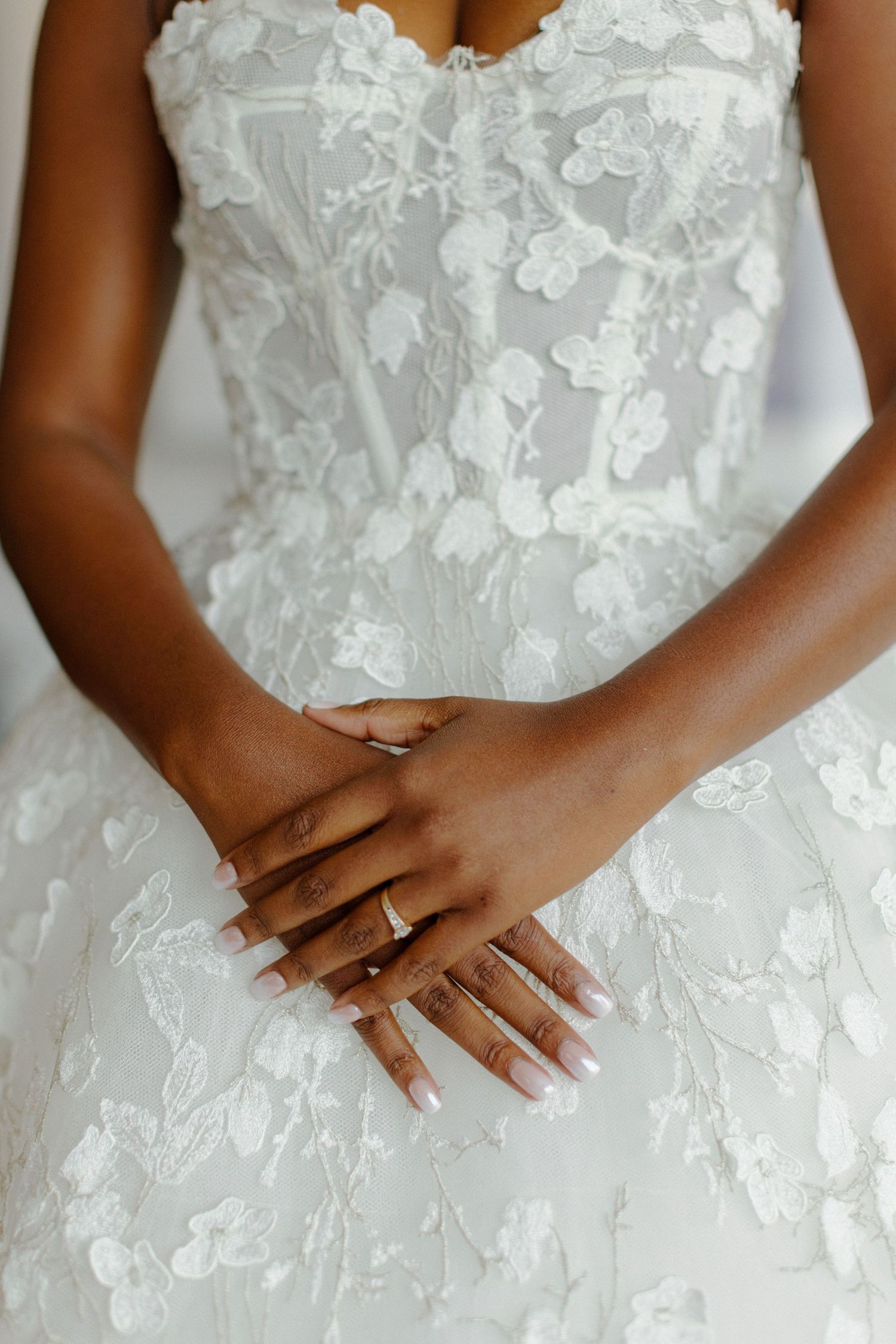Close-up of delicate white floral lace wedding dress detail and clasped hands with manicured nails.