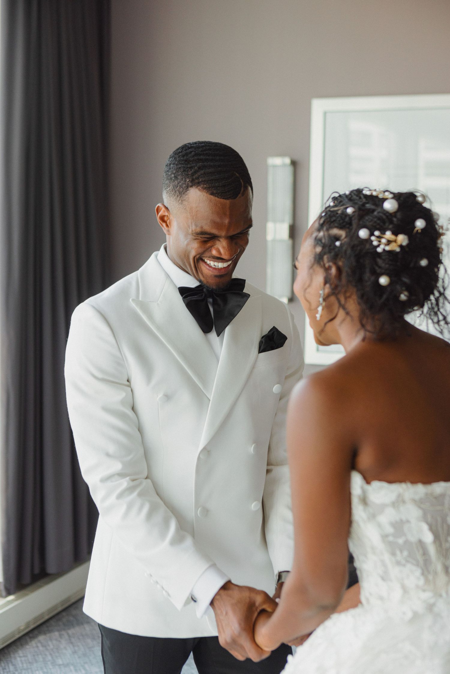 A tender moment shared between a couple in formal wedding attire in a sunlit room.