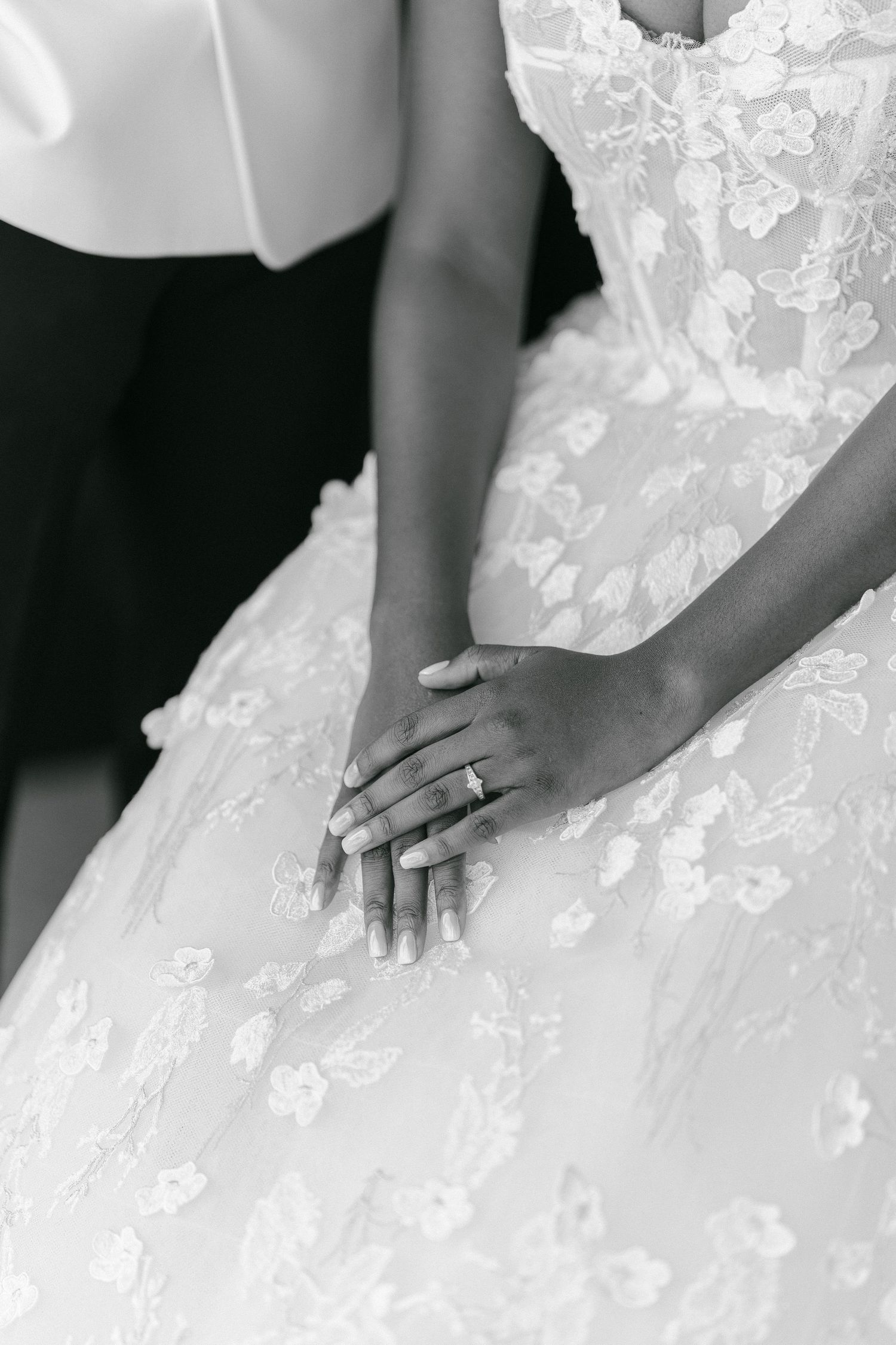 Close-up of wedding rings and hands resting on a detailed lace wedding gown.