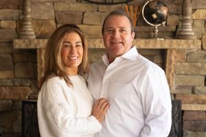 A couple poses together in front of a stone fireplace with a decorative clock on the wall.