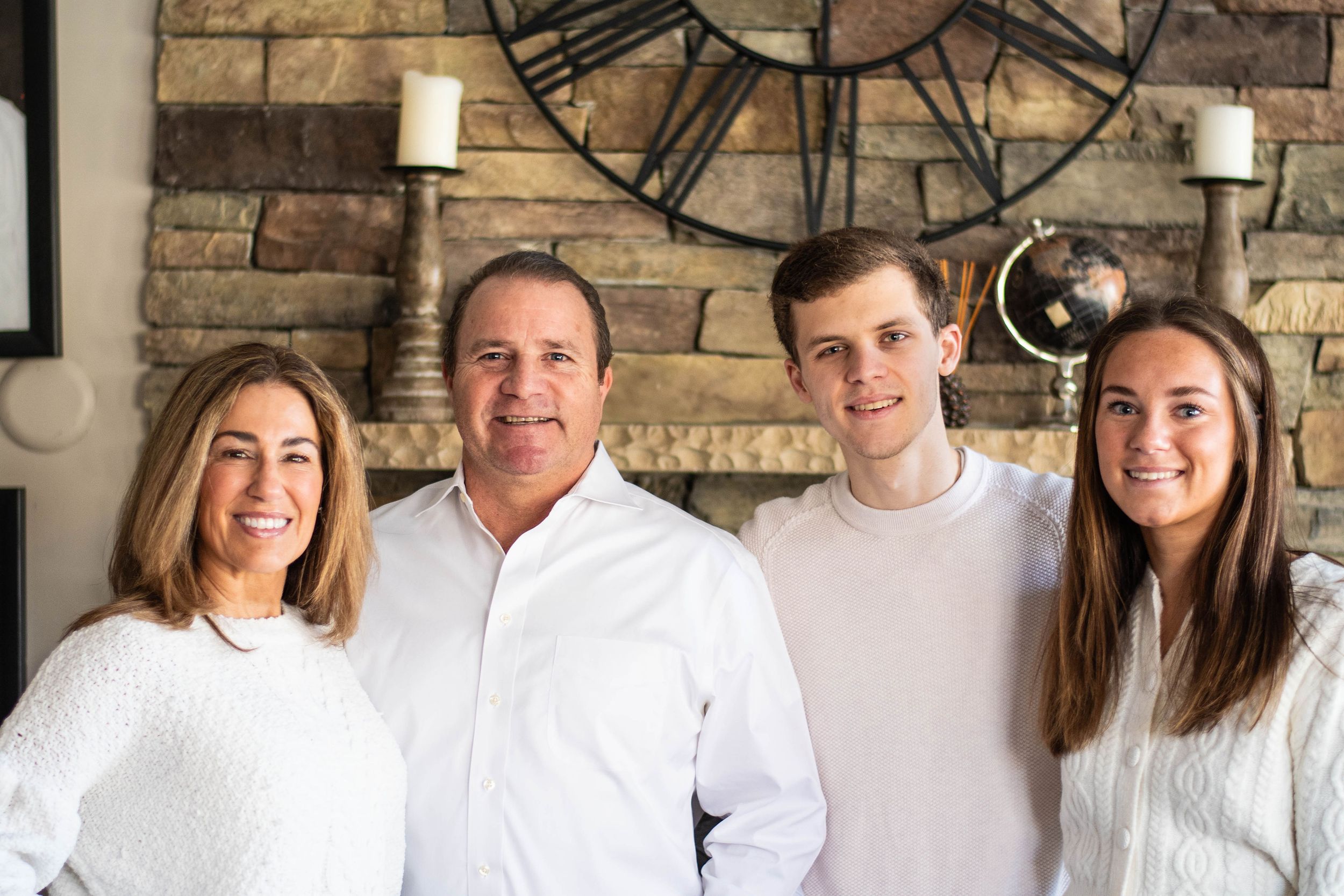 A family group poses together indoors against a stone wall with a large decorative clock.