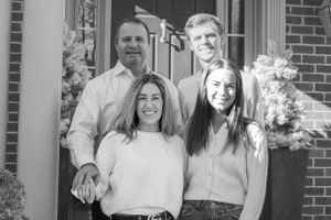 Black and white outdoor portrait of a family of three standing together near a brick building entrance.