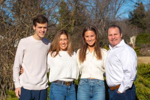 A family of four poses outdoors on a sunny day wearing coordinated white and blue outfits.