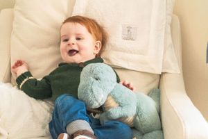 Relaxing on a cream colored cushion with a blue plush dinosaur toy.