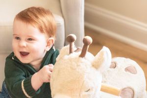 Playfully interacting with a cream colored plush giraffe toy while wearing a dark green sweater.