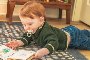A young reader lying on a patterned rug engages with a picture book.