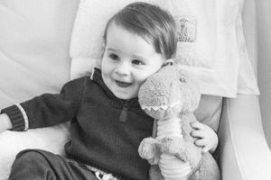 A happy child with a stuffed toy smiles while wearing a dark sweater.