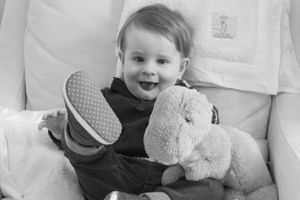 Black and white image showing joy while holding a plush toy on a light colored chair.