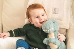 A joyful moment on a couch with a plush blue dinosaur toy and hunter green sweater.