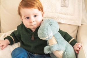 Sitting comfortably with a blue dinosaur plush toy against a white backdrop.