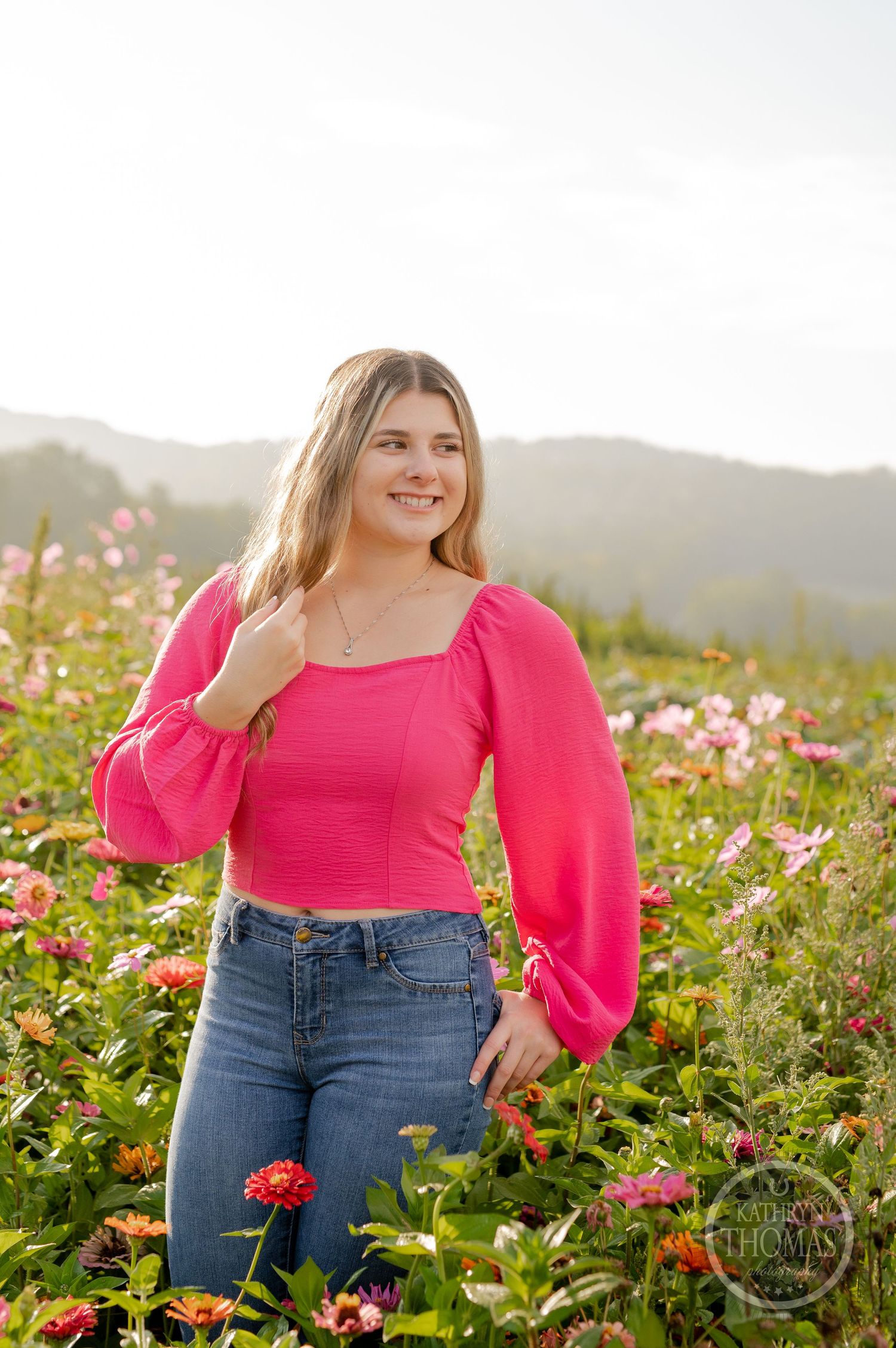 Someone wearing a bright pink top and jeans poses in a garden of colorful flowers.