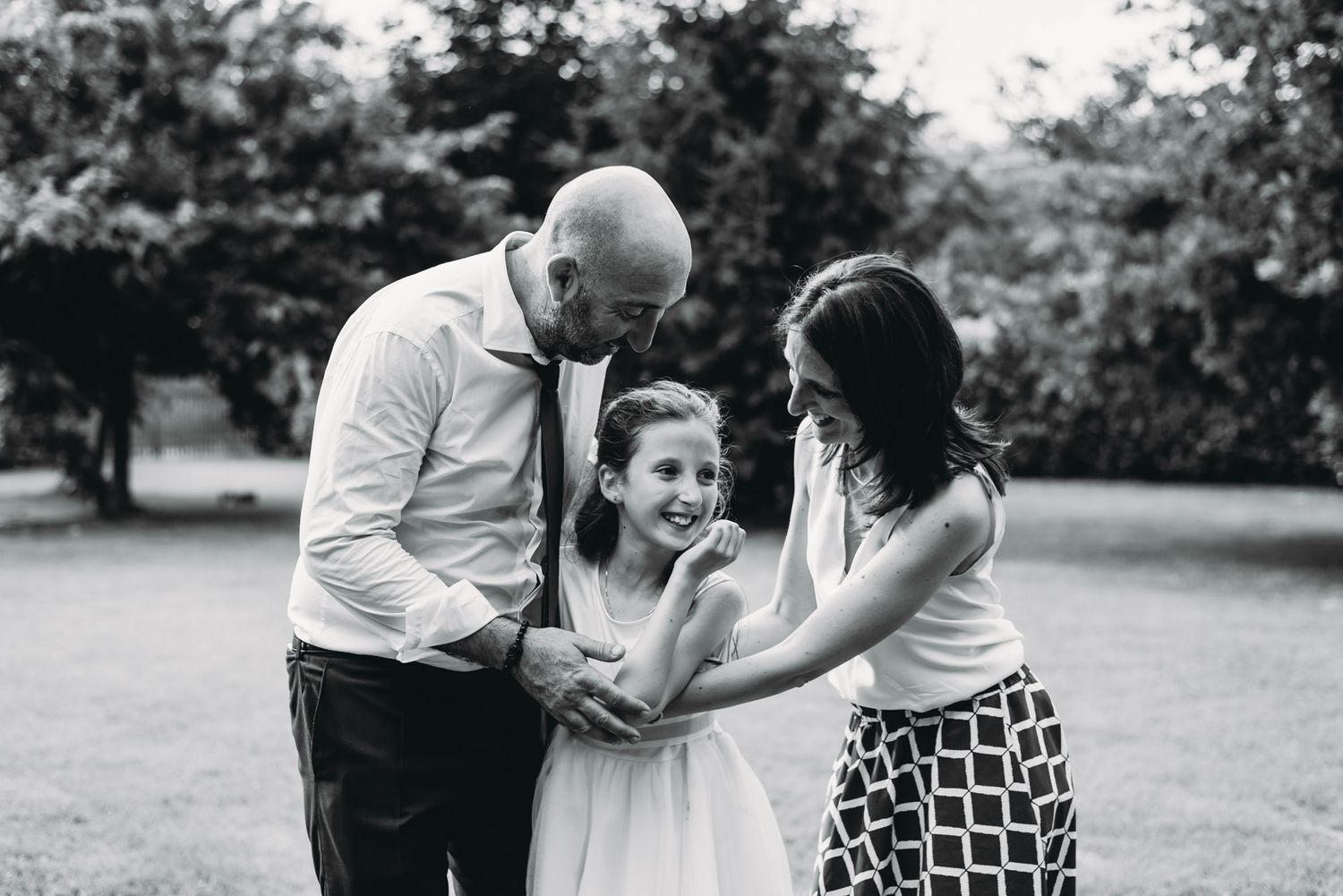 A black and white candid family portrait captured in a park setting.