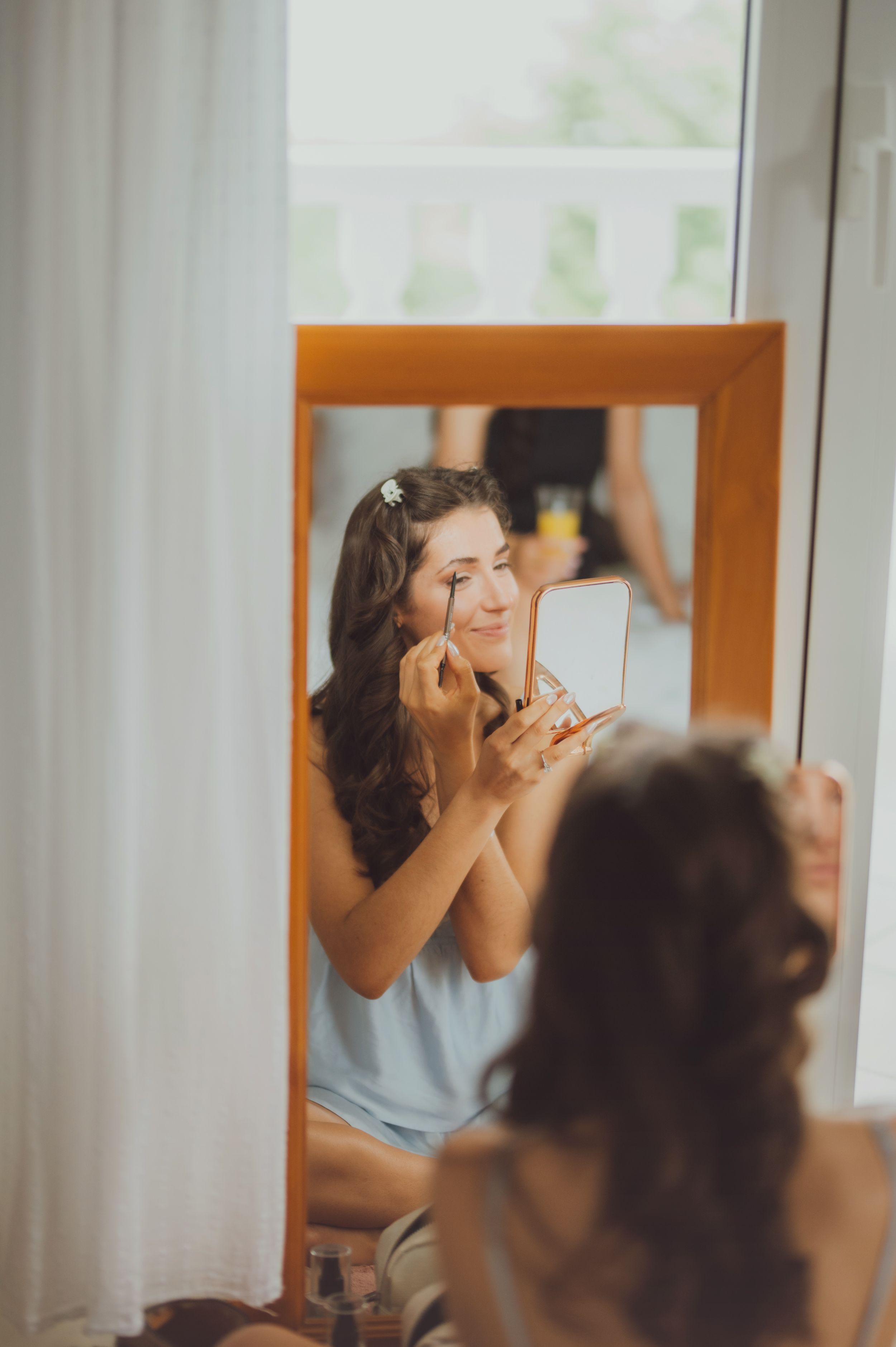 Person applying makeup in front of a bathroom mirror wearing a light blue shirt.
