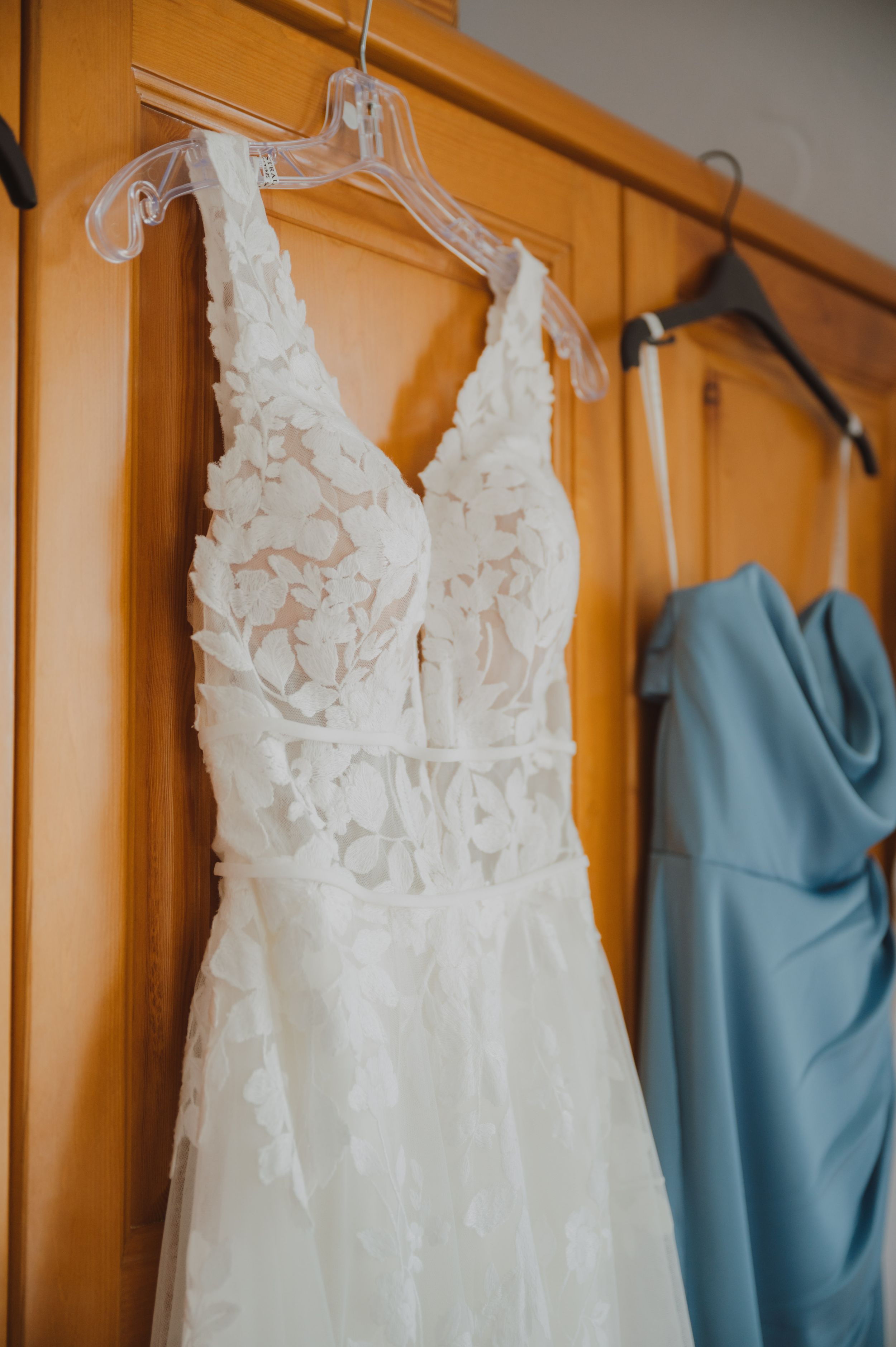 White wedding gowns and light blue bridesmaid dresses hanging on wooden hangers.