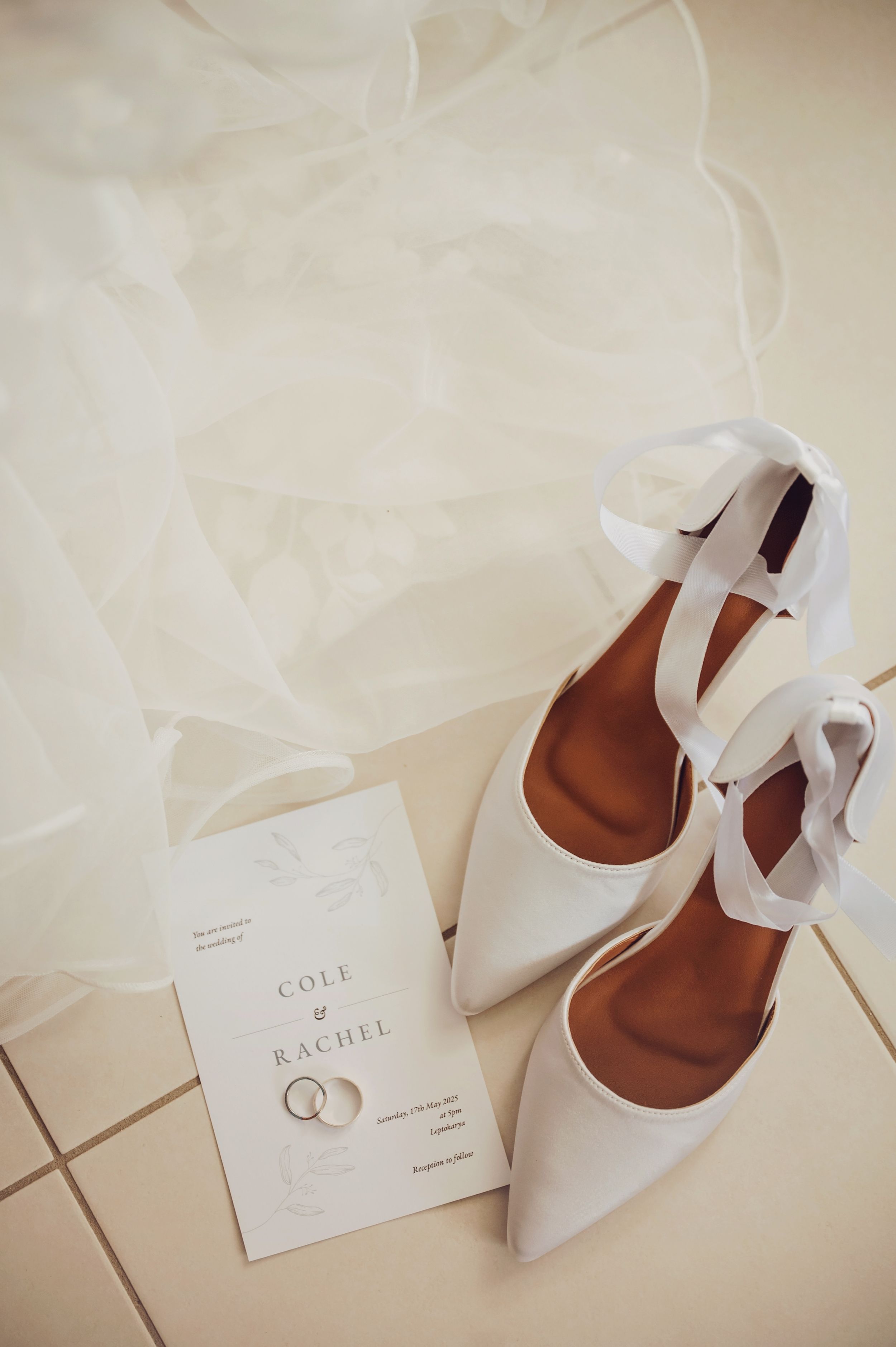 White wedding shoes and invitation cards arranged on a light beige surface.