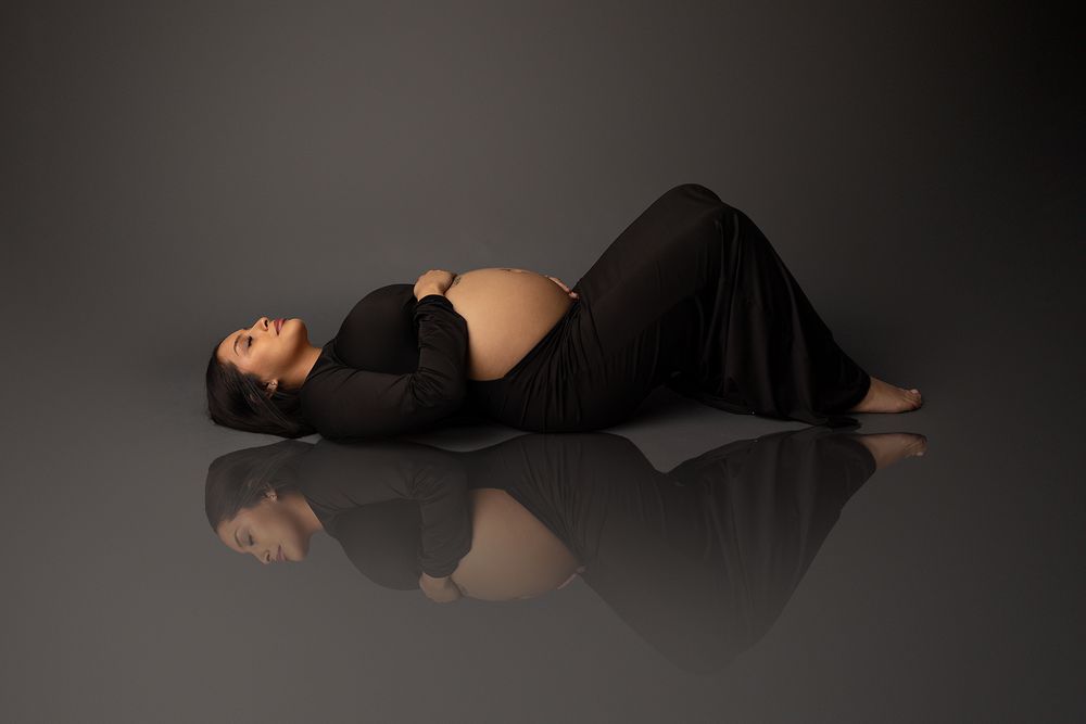 Artistic silhouette photograph of a figure in black dress lying down against dark background.
