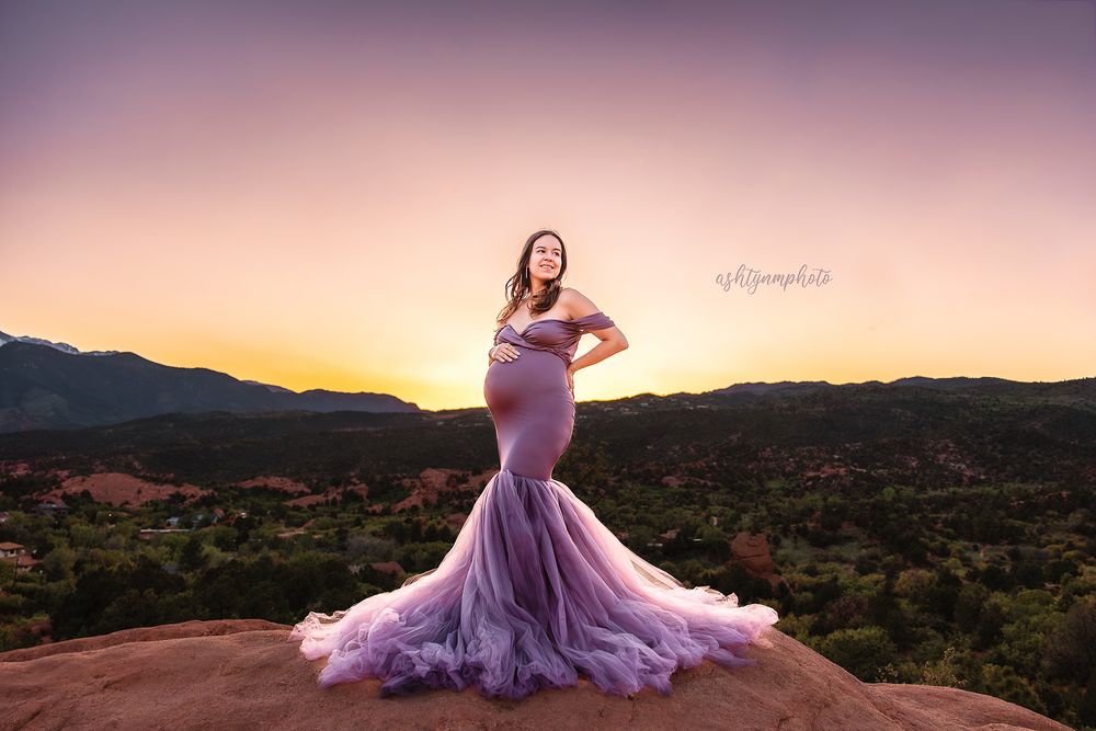A purple ballgown dress flows elegantly against a desert mountain landscape at sunset.