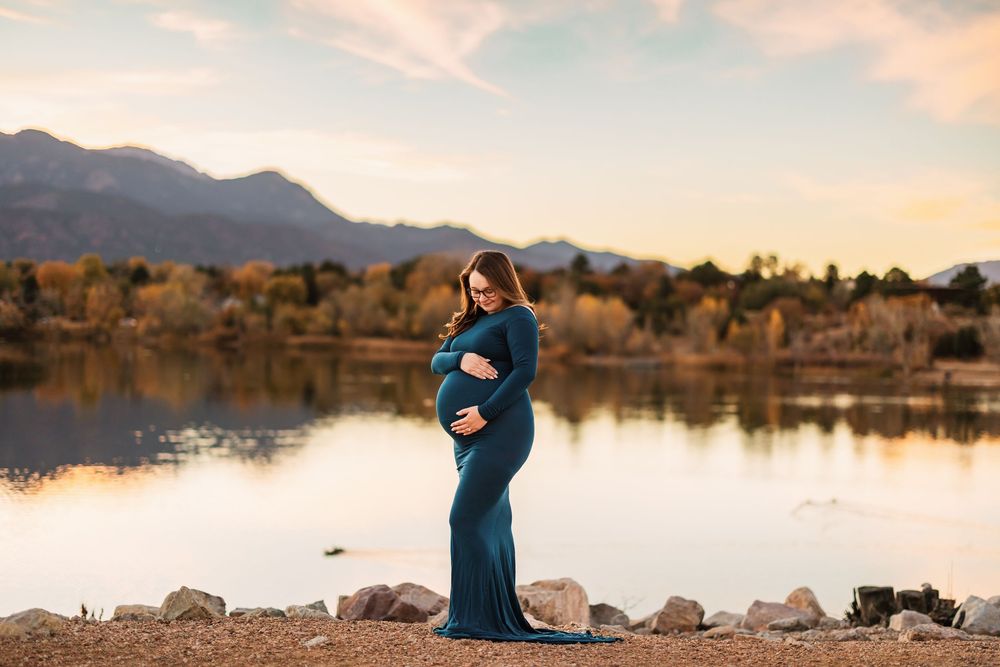 Scenic mountain lake landscape at sunset with silhouettes standing on rocky shore in teal dress.