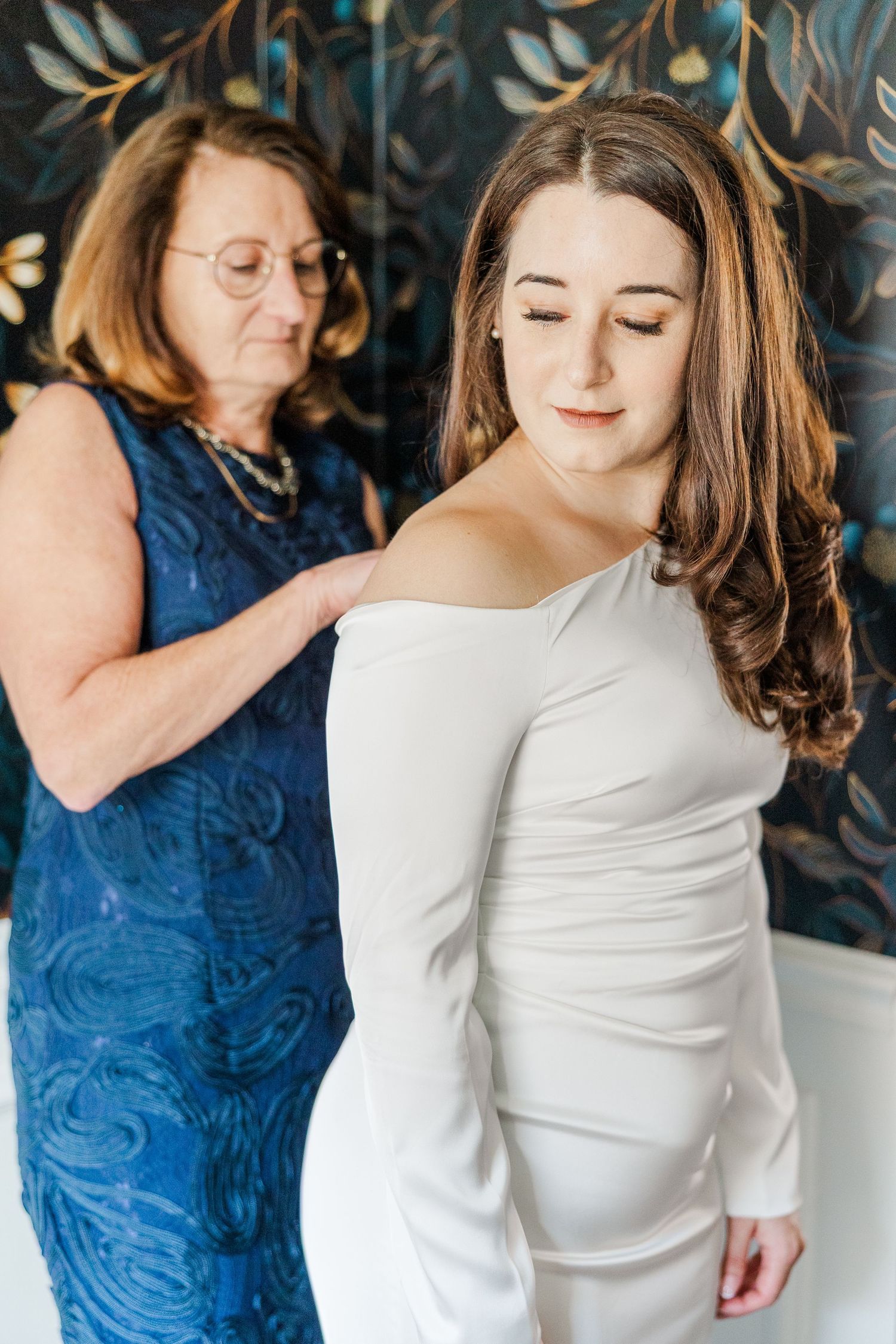 A couple in white and blue outfits share an intimate moment during a photoshoot against a blue textured background.