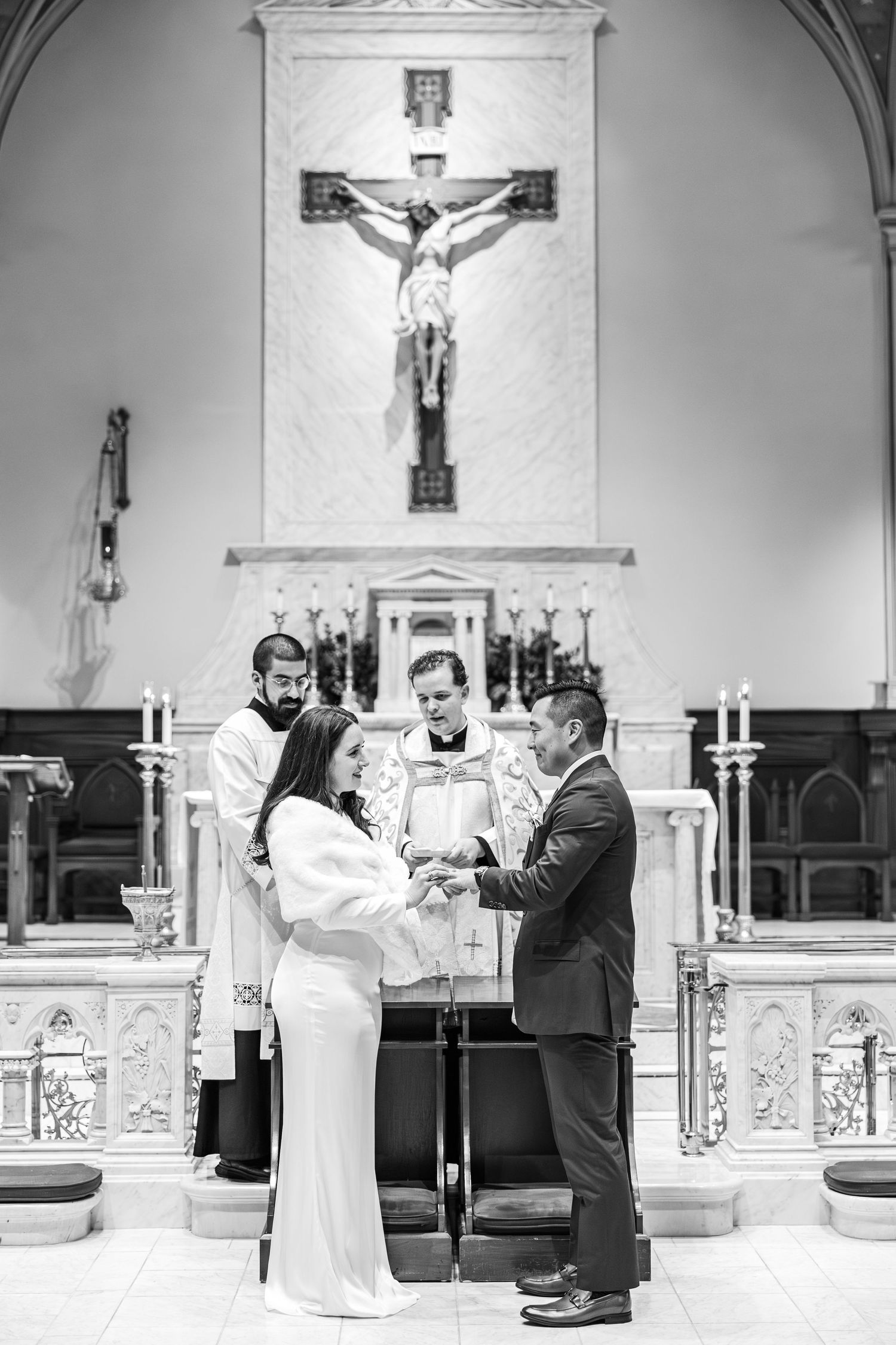 A wedding ceremony takes place in a traditional Catholic church with a crucifix on the altar.