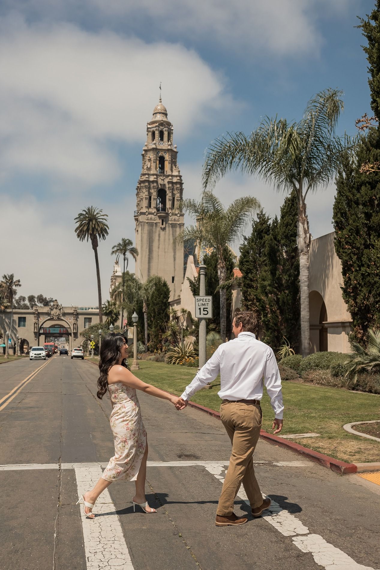 A couple walks hand in hand down a path near the historic California Tower in Balboa Park, San Diego.