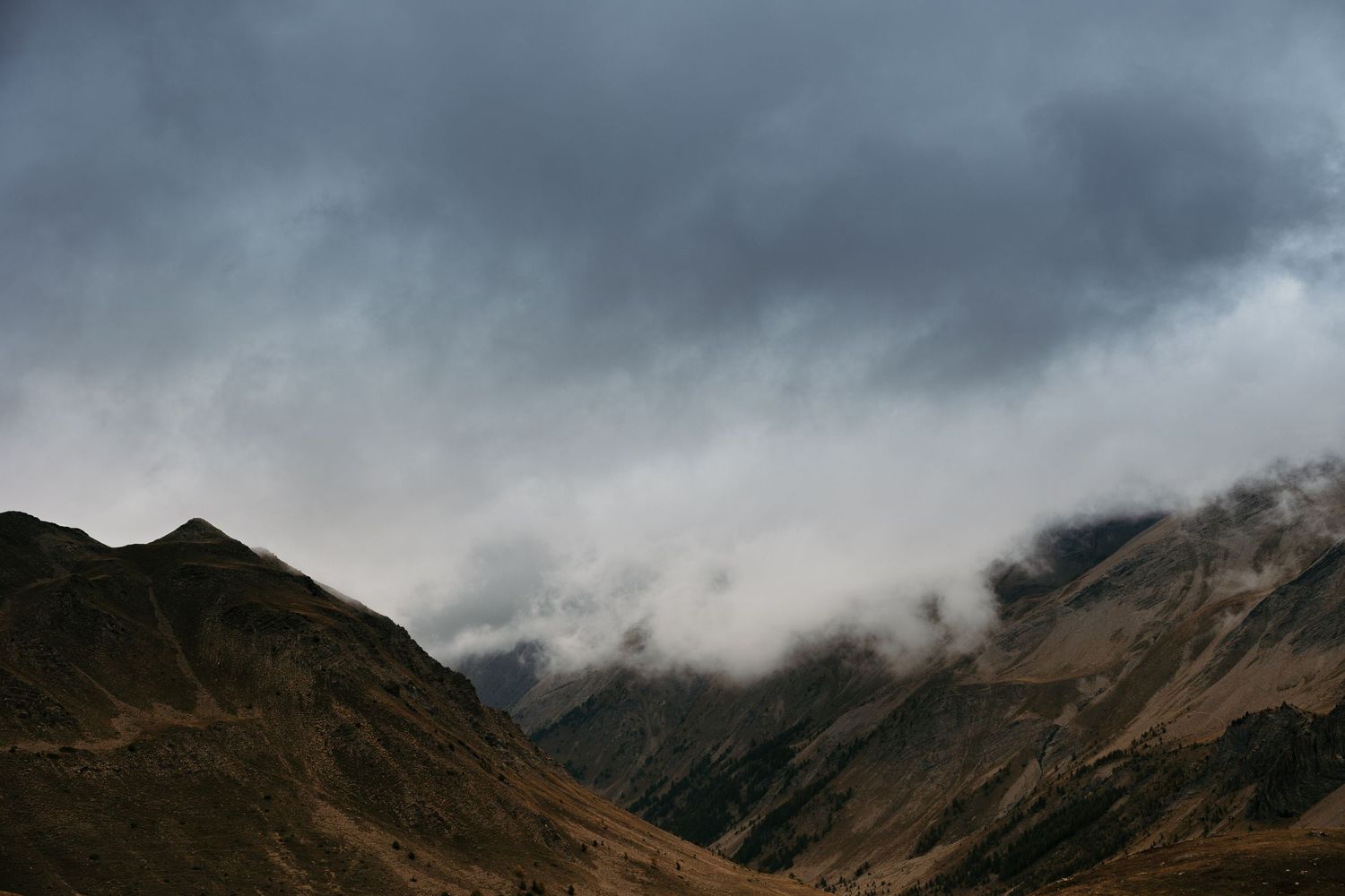 Dramatic storm clouds roll over rugged mountain peaks in moody overcast weather.