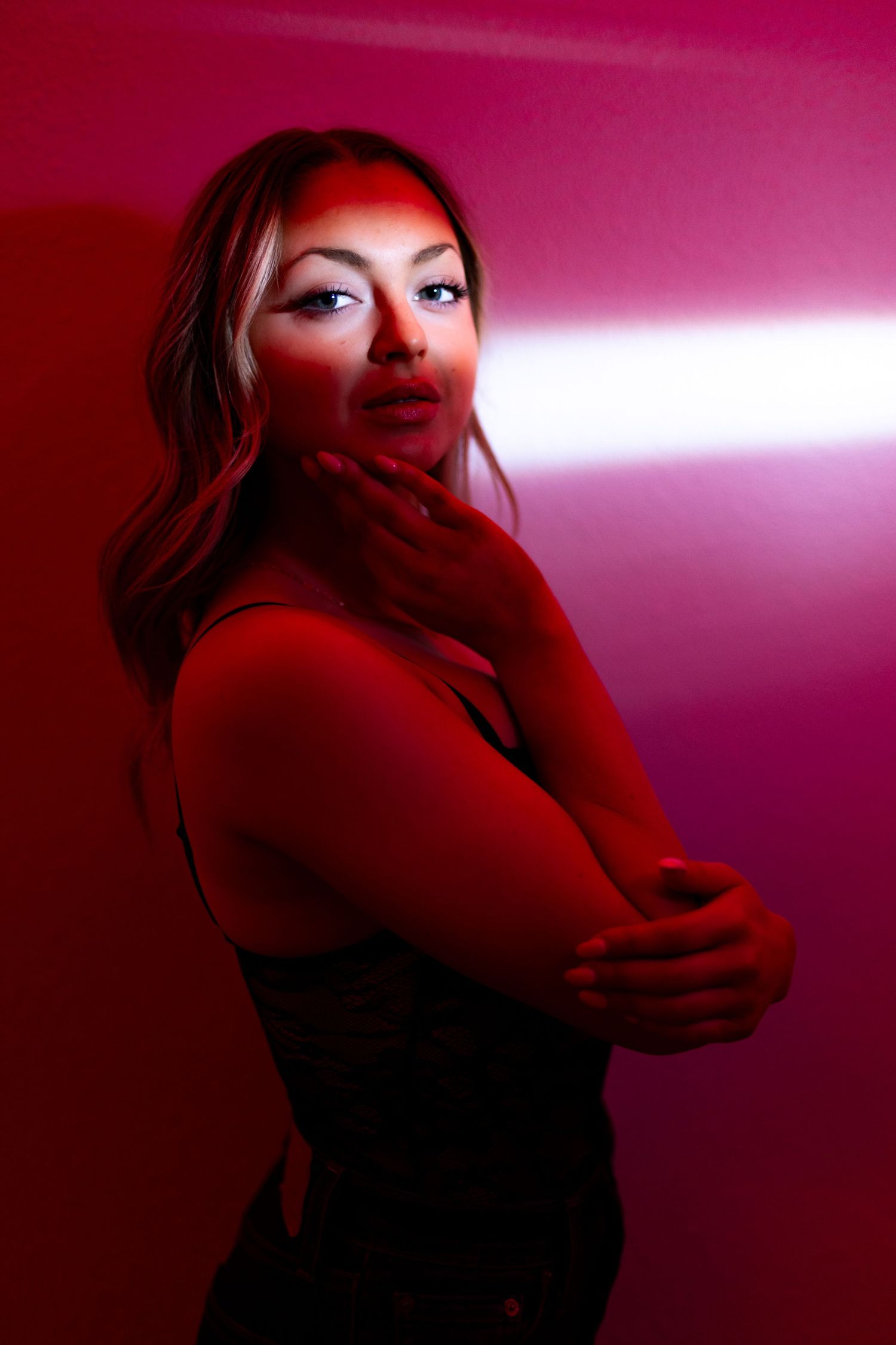 Artistic portrait in red lighting showing dramatic pose against vibrant background with moody atmosphere.