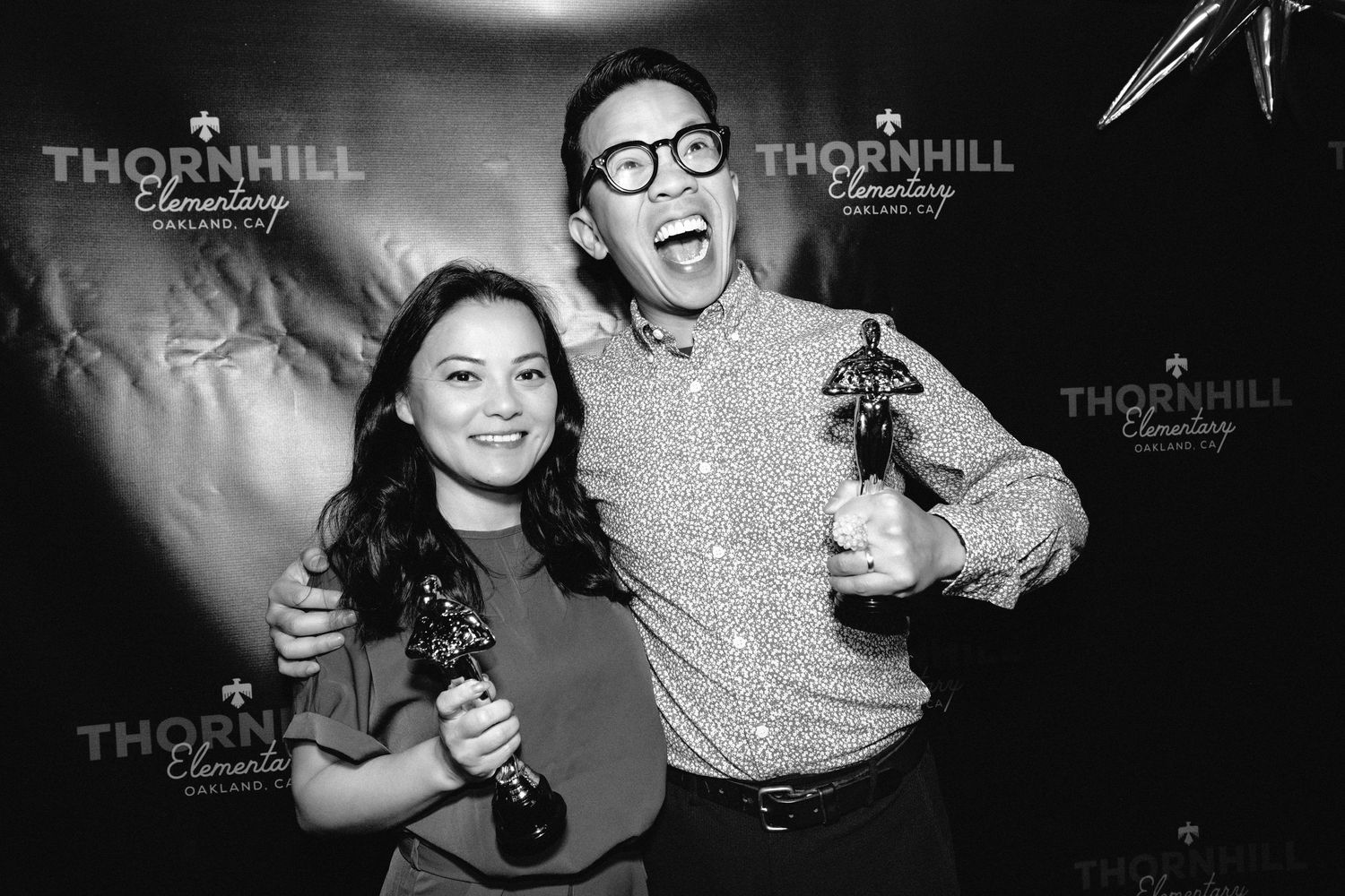 Two people pose together with trophies in front of a Thornhill branded backdrop at an event.