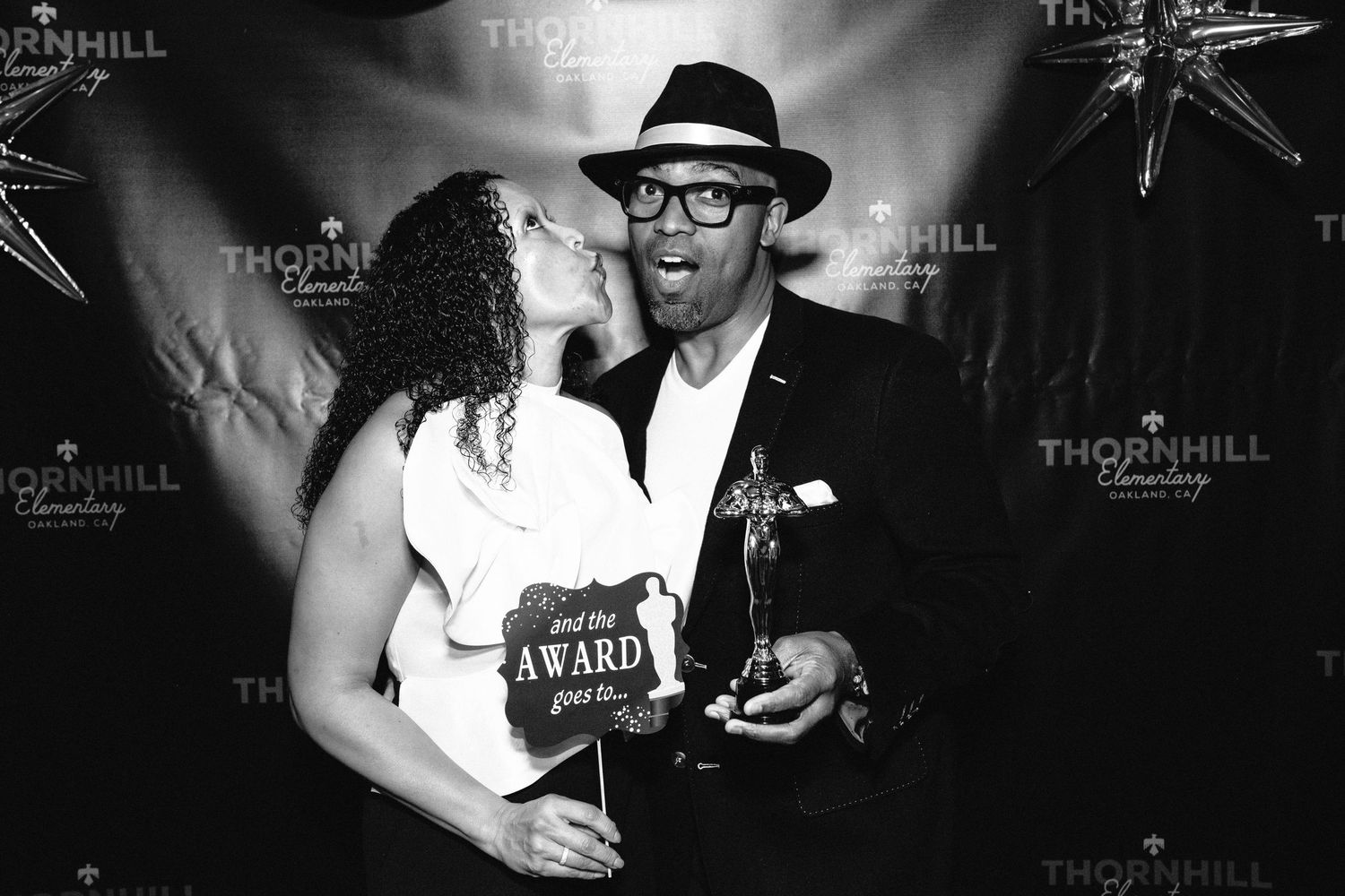 A black and white photo of a person wearing a fedora hat at a formal event with a dark backdrop.