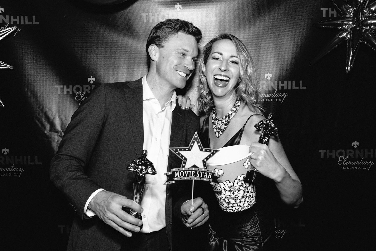 Two people laugh together while holding drinks at a nightclub event in black and white photography.