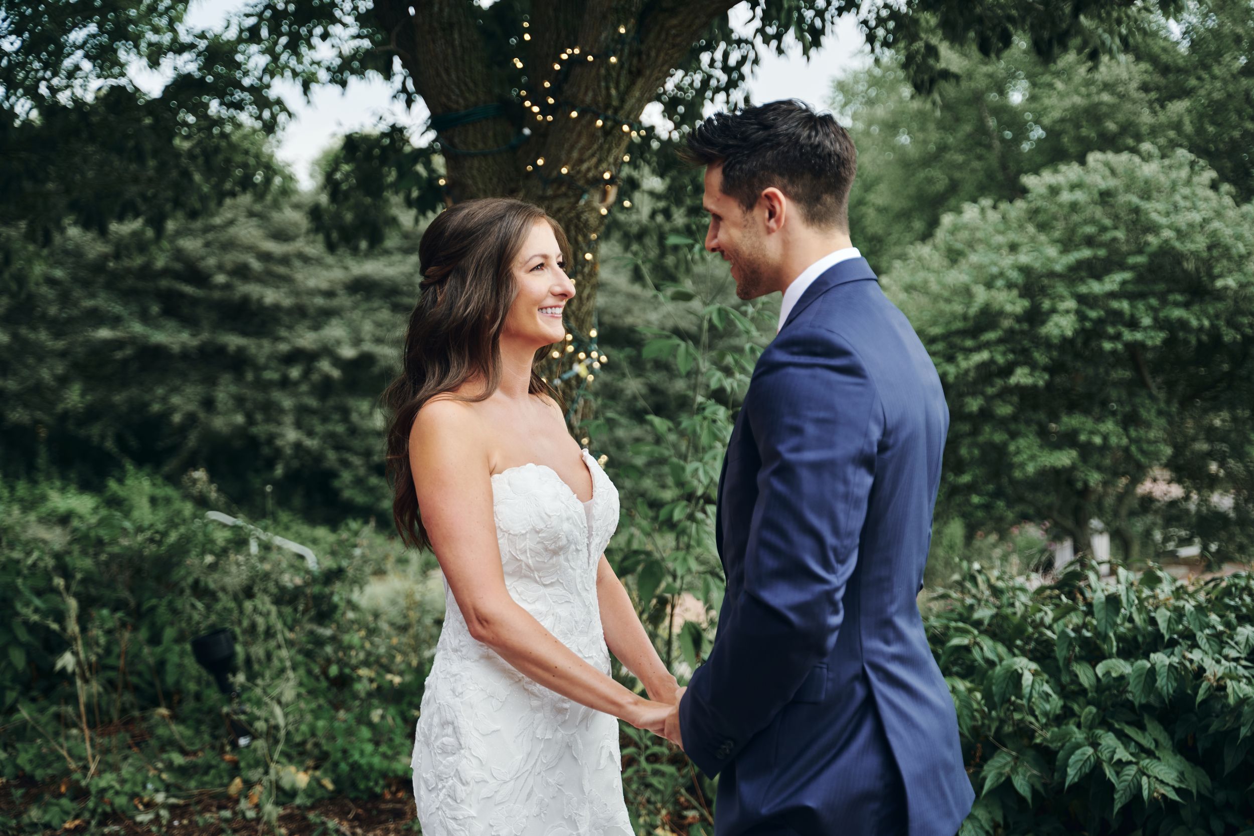 Couple in wedding attire share intimate moments while standing in a lush green garden setting.