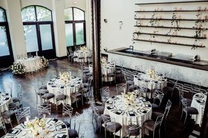 Elegant wedding reception venue with white tablecloths, floral centerpieces and rustic wooden beams in a spacious hall.