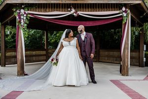 A couple shares a romantic moment under a wooden pergola decorated with pink and white floral arrangements and draping.