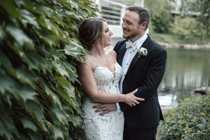 A romantic wedding couple embraces by a serene lake surrounded by lush greenery on their special day.