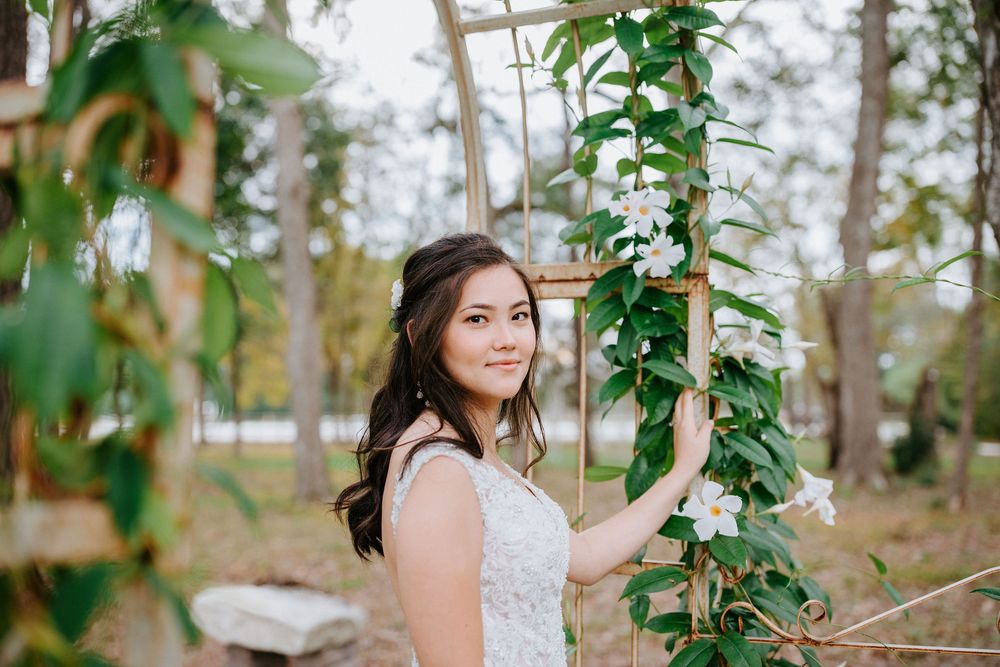 Woman in white lace dress poses elegantly among flowering vines and greenery in an outdoor garden setting.