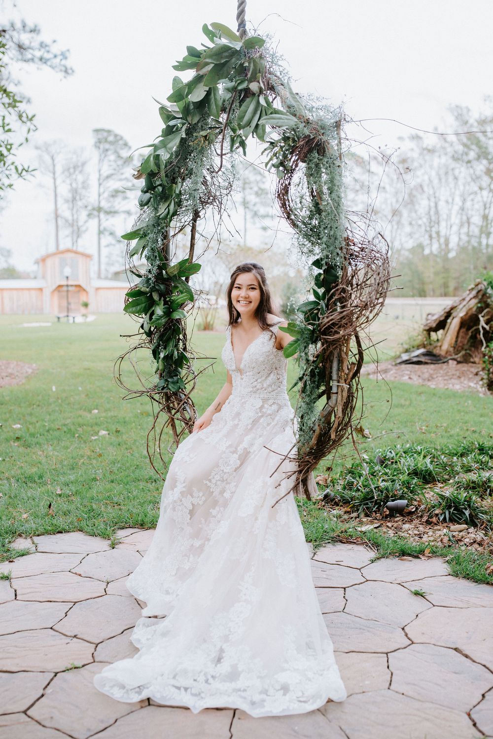 A beautiful wedding dress is showcased under a rustic arch decorated with greenery and vines on a stone patio.