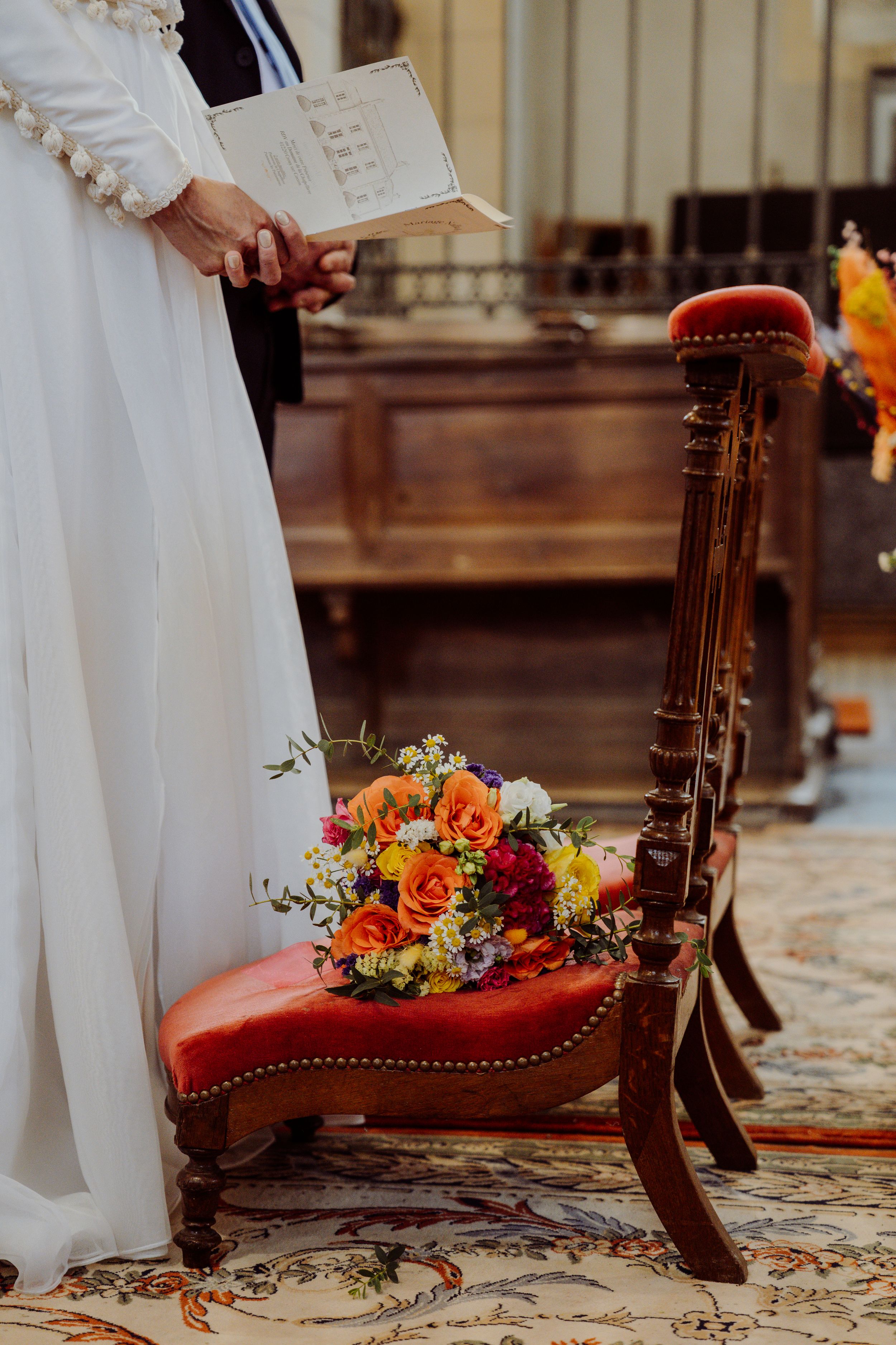 Antique red velvet chair with colorful floral bouquet arrangement placed on ornate patterned carpet.