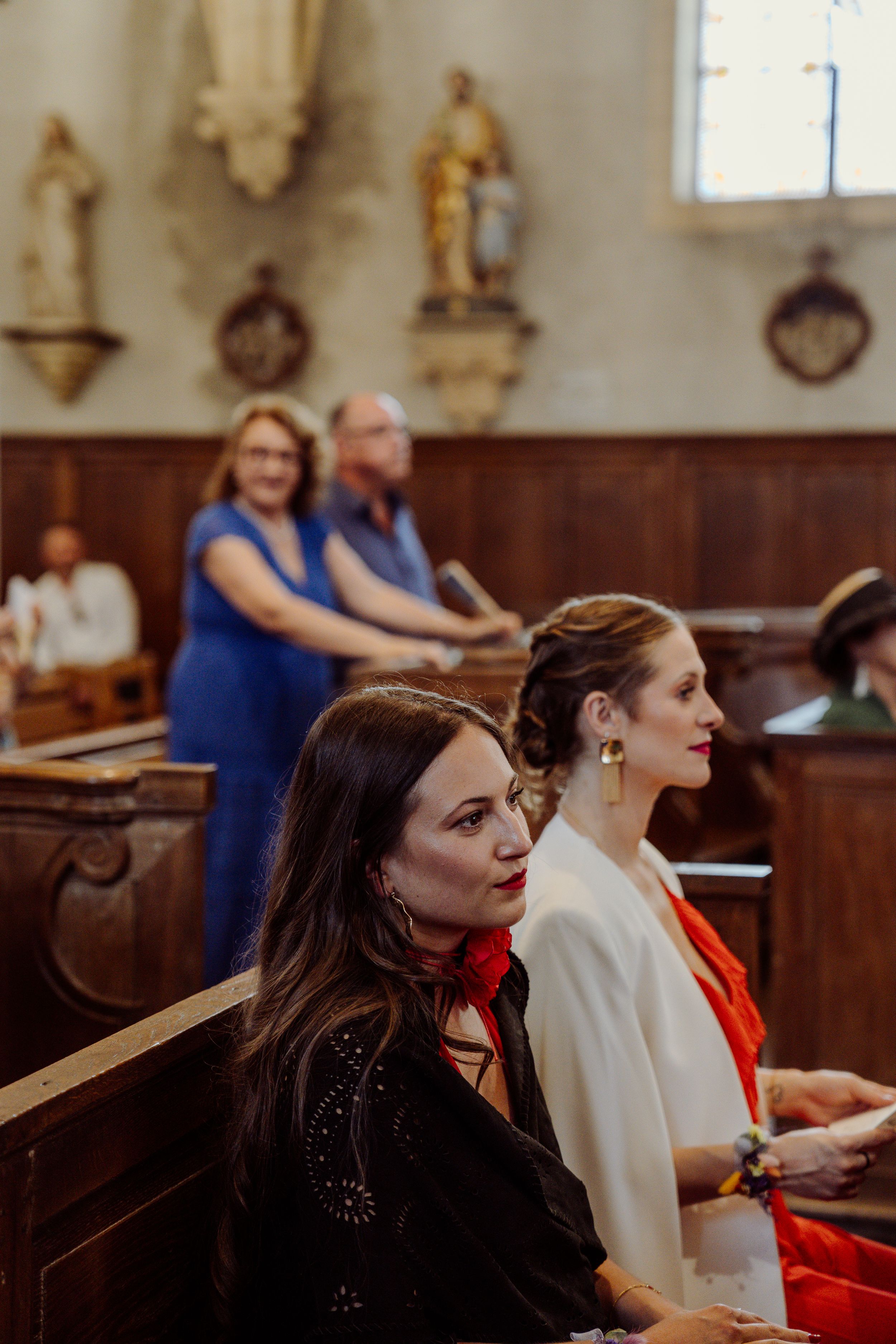 People seated in wooden church pews during a service with decorative wall ornaments visible in the background.