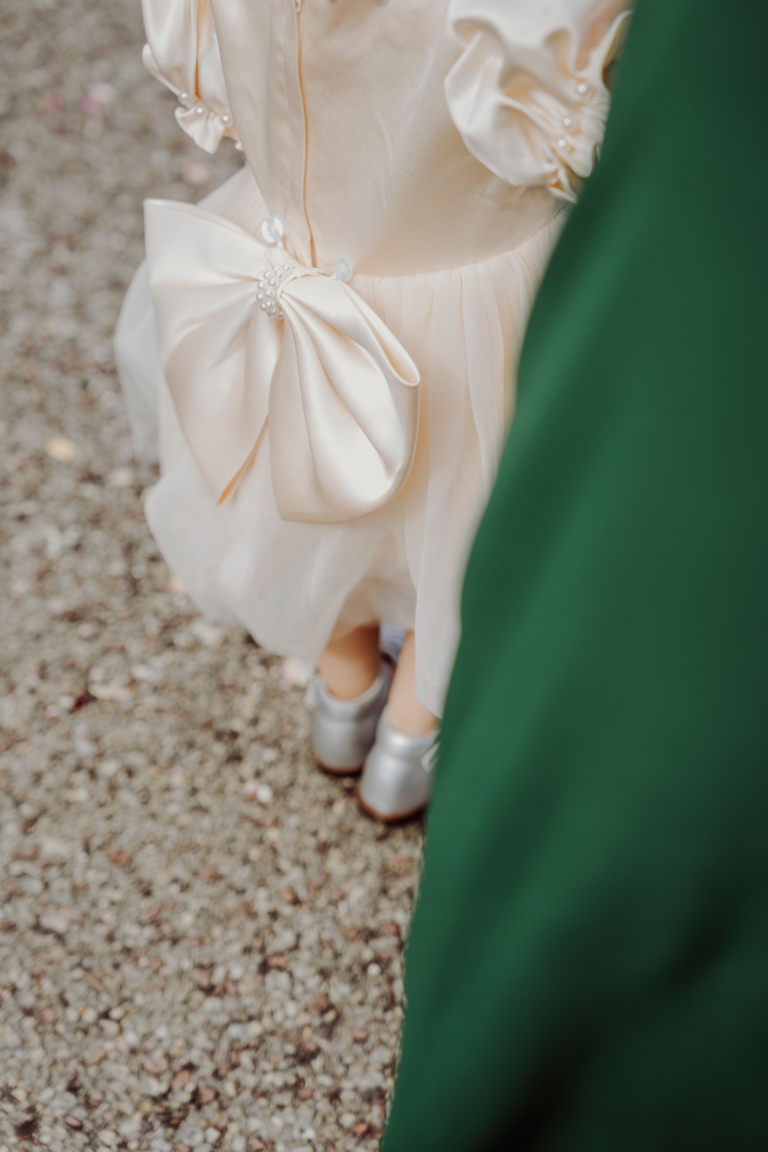 Close-up detail of a white wedding dress with delicate bow and fabric details against a green background.