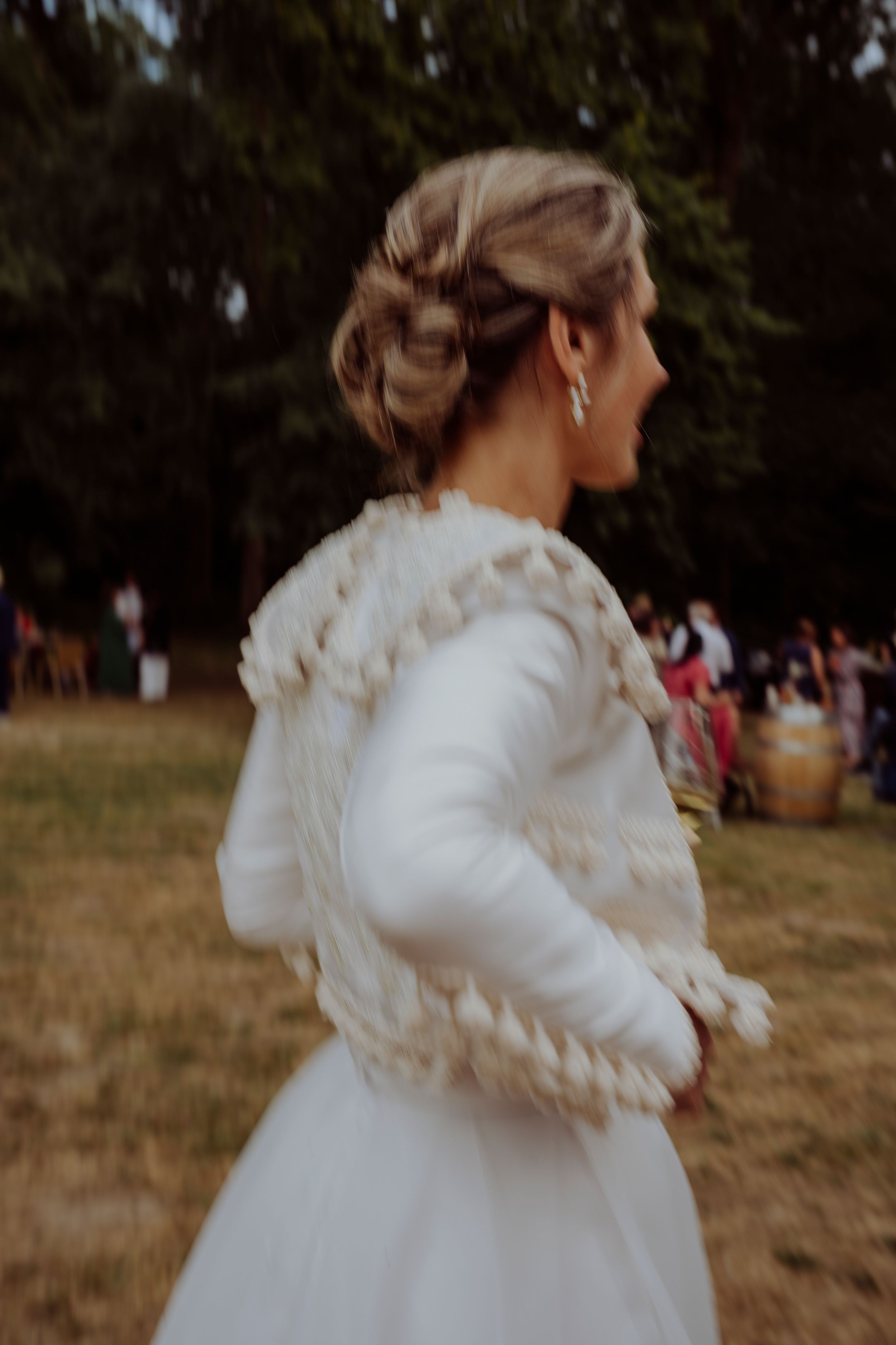 A person in a white wedding dress with ruffled details stands outdoors during a celebration.