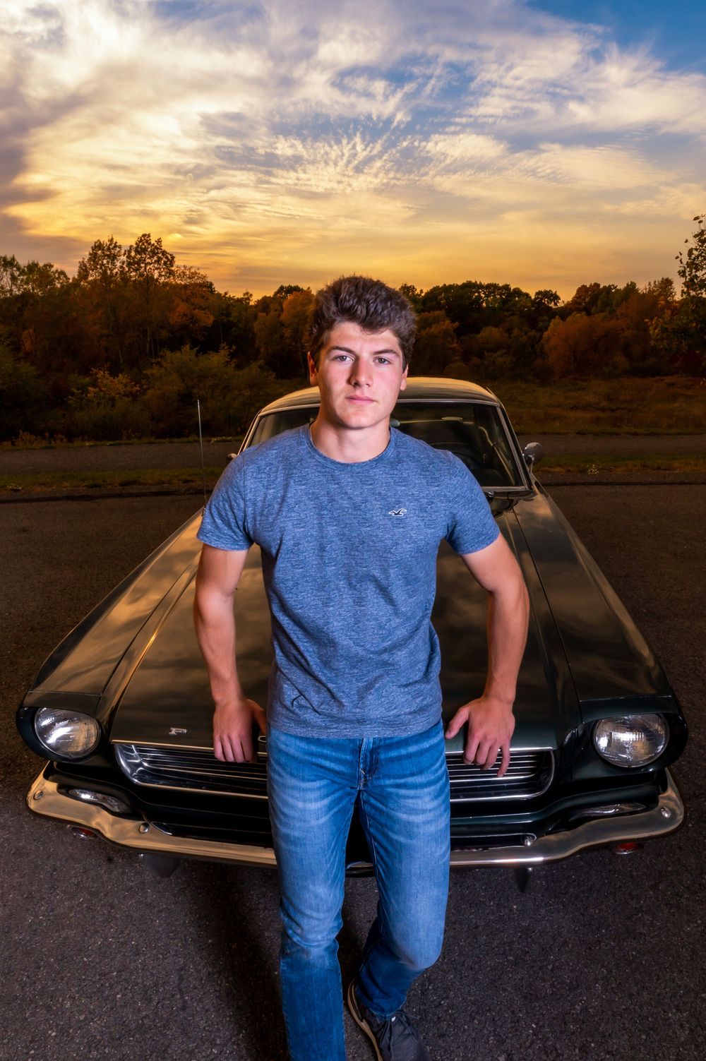 A classic vintage Ford Mustang with chrome bumper parked at sunset with dramatic orange sky backdrop.